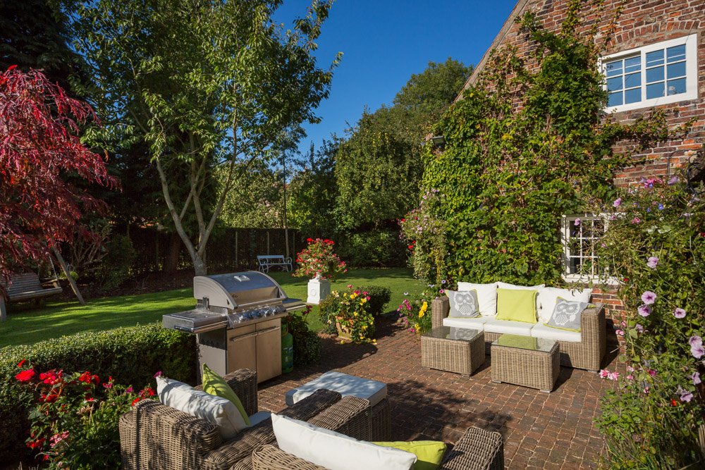  patio area with woven furniture, large BBQ grill, neat lawn up to the hedge, rear of house covered in ivy  