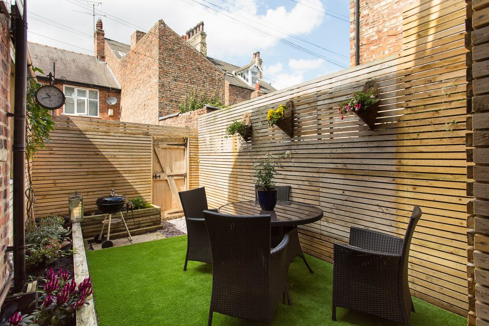  small courtyard with Astroturf, high wooden fencing and outdoor table and chairs  
