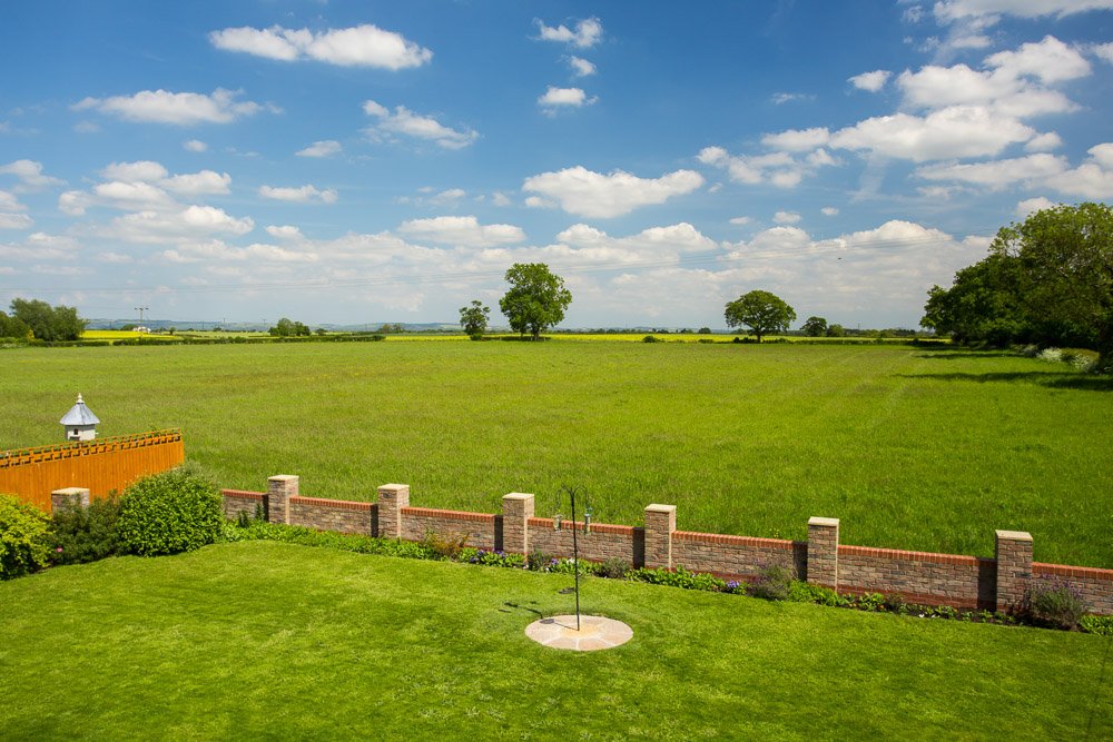  grass lawn with bird feeder in the centre, over a small brick wall fields for miles 