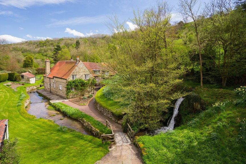  elevated image coutryside cottage surrounded by hiilside and trees with river running alongside 