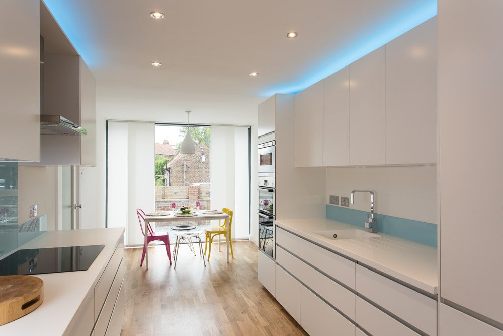  kitchen diner with wooden flooring, large window, white units, colourful dining chairs  