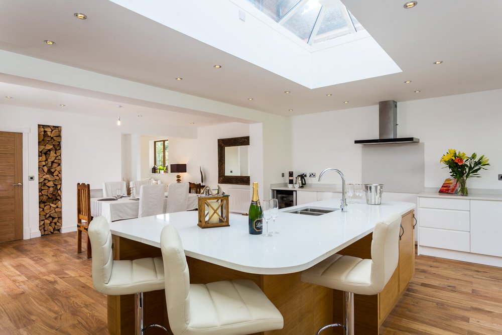  modern white kitchen with breakfast bar with messy cream leather stools  and champagne bottle on table  
