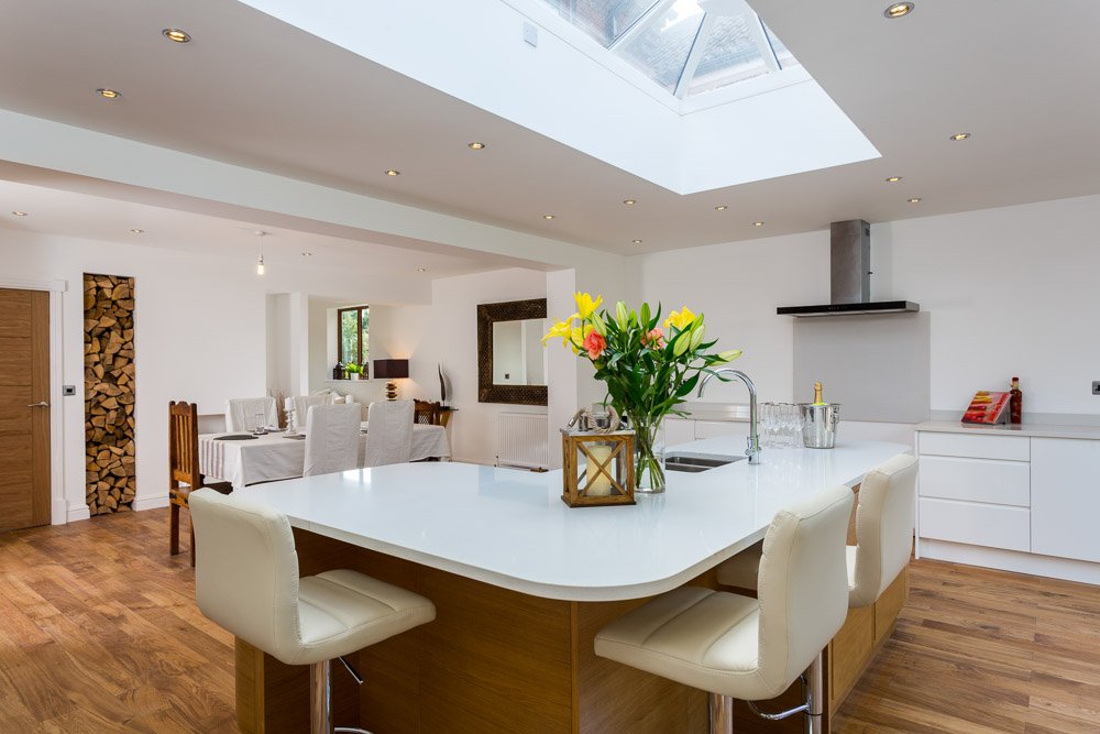  modern white kitchen with breakfast bar with  cream leather stools  and flowers 