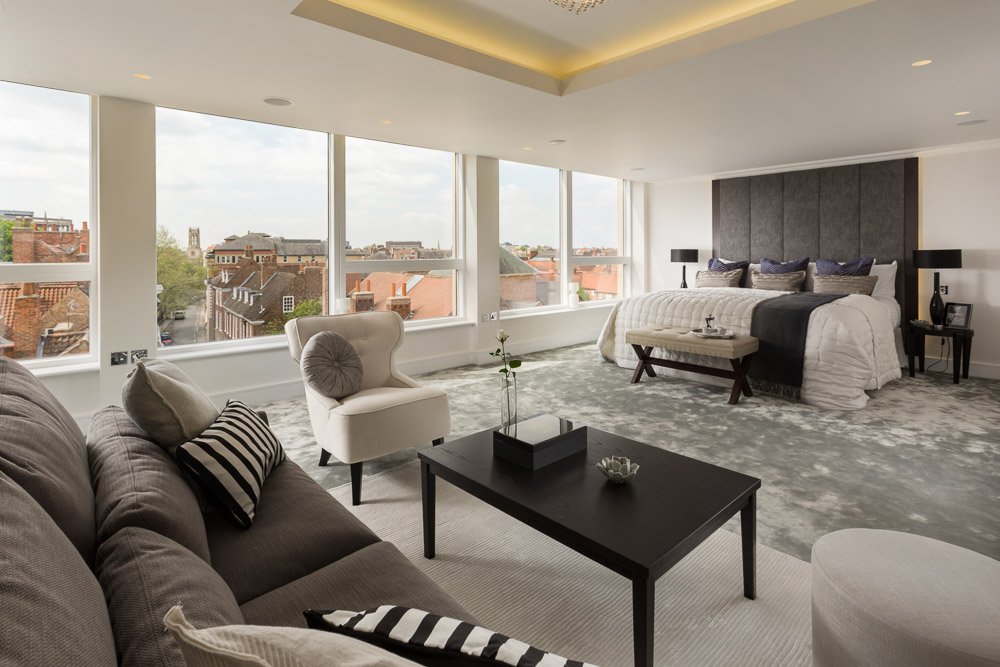  very modern apartment bedroom with very large bed and grey sofa, views above York city from the panoramic windows 