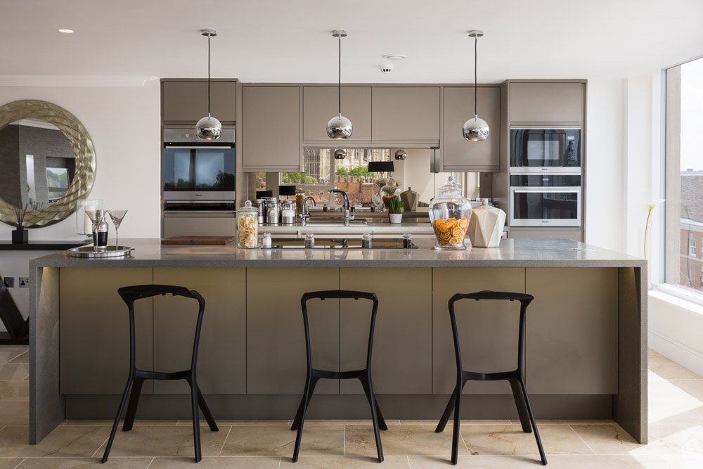  same modern kitchen with grey cupboards and grey marble worktops, furnished with black metal frame chairs and appliances on the counters 
