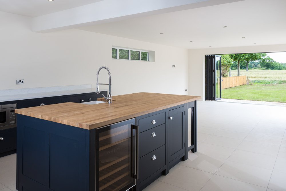  modern kitchen/dining room with dark navy cupboards and light wood worktops, bi fold doors lead out to gardens 