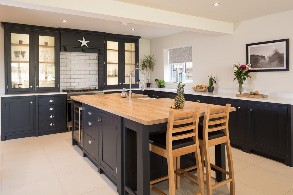  same shaker style kitchen with wooden worktops and navy units, furnished with appliances and two tall wooden chairs as a breakfast seating area  