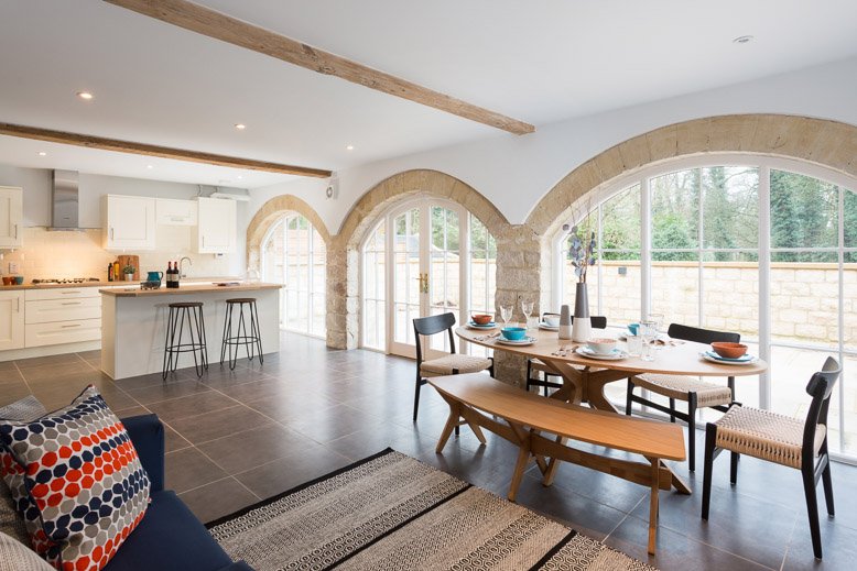  south facing kitchen/diner with high ceilings and large arched windows, round wooden kitchen table, blue sofa and two metal stools at the kitchen island 