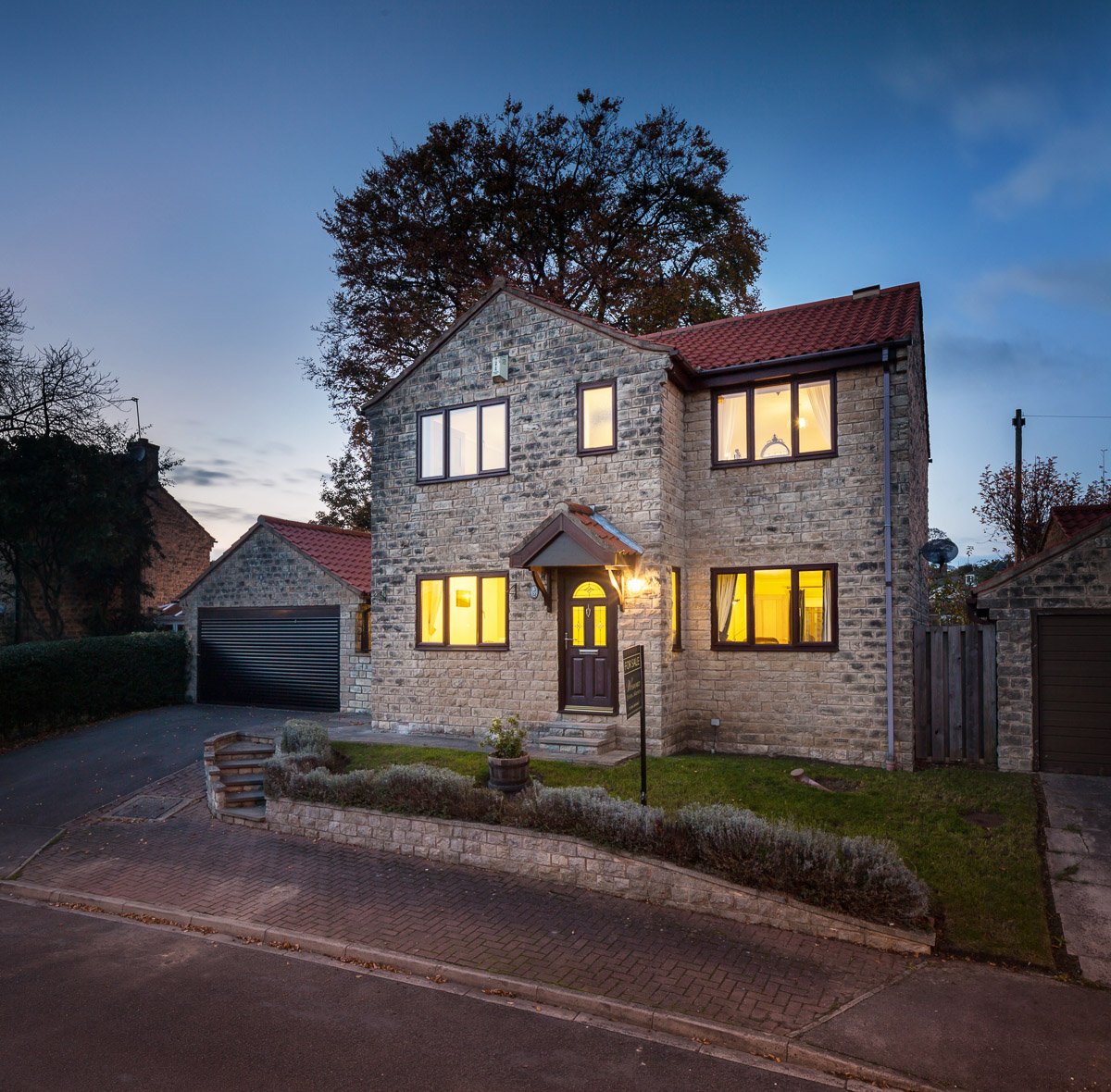  front elevation of grey brick house at dusk with for sale board 