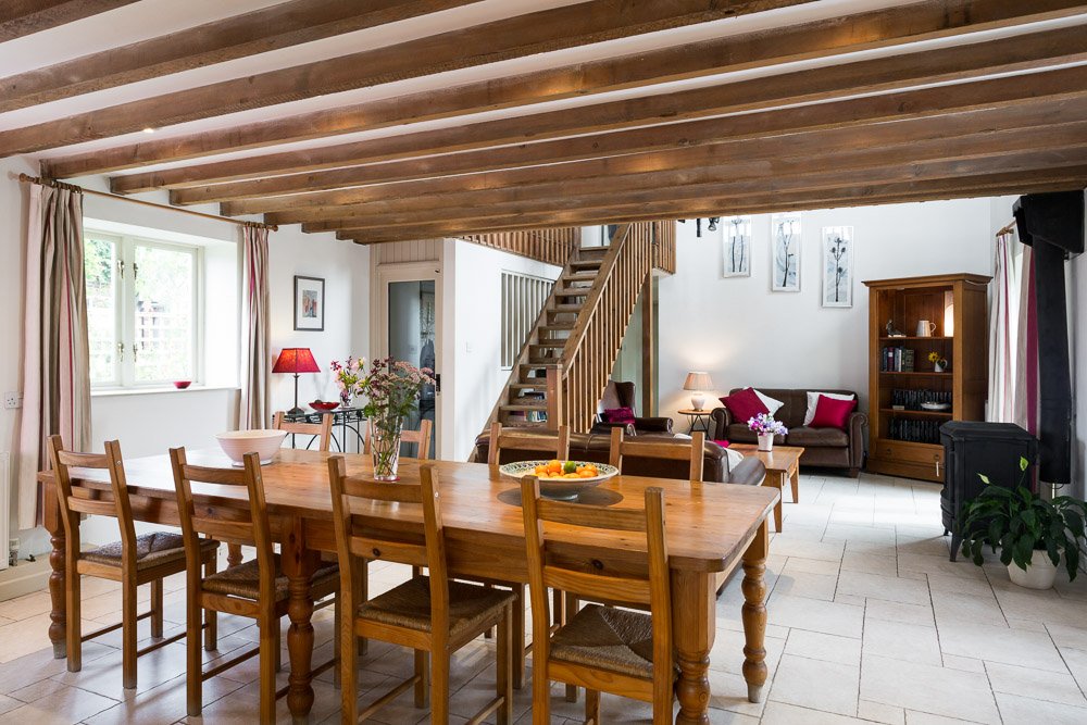  beamed ceiling dining room with wooden dining table, sofa and stair case in background 