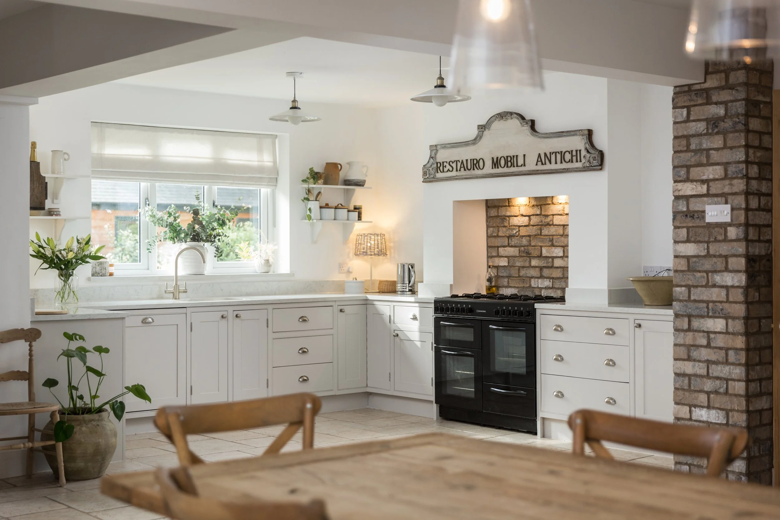 shallow depth of field image across dining table looking at white kitchen units with large black range cooker