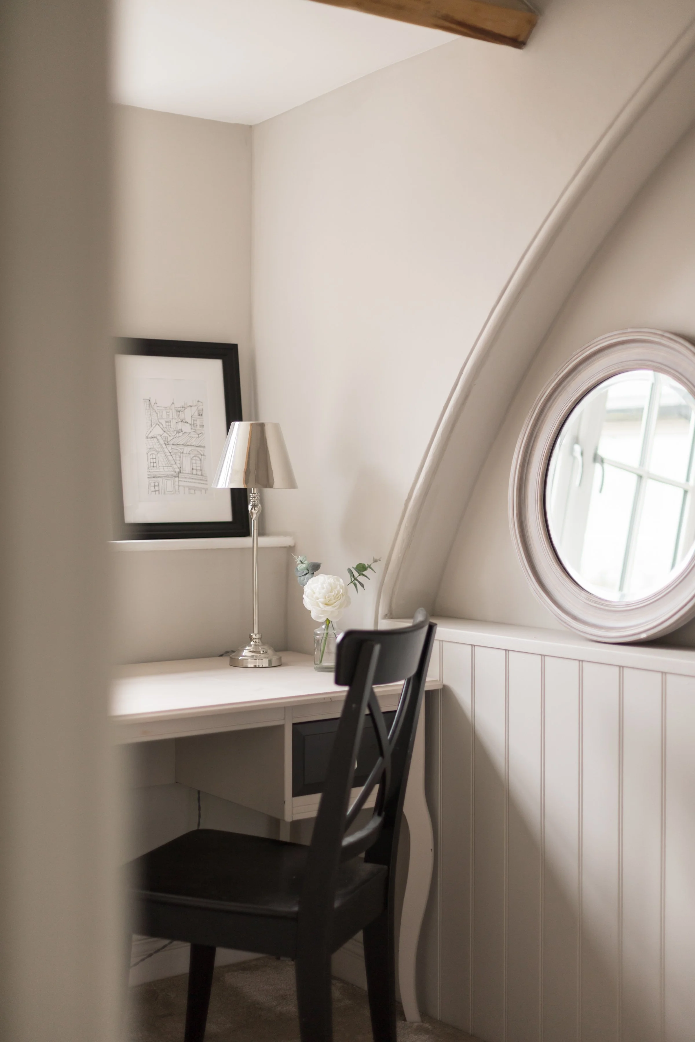 portrait image of a black wooden chair sat at a white desk with round mirror