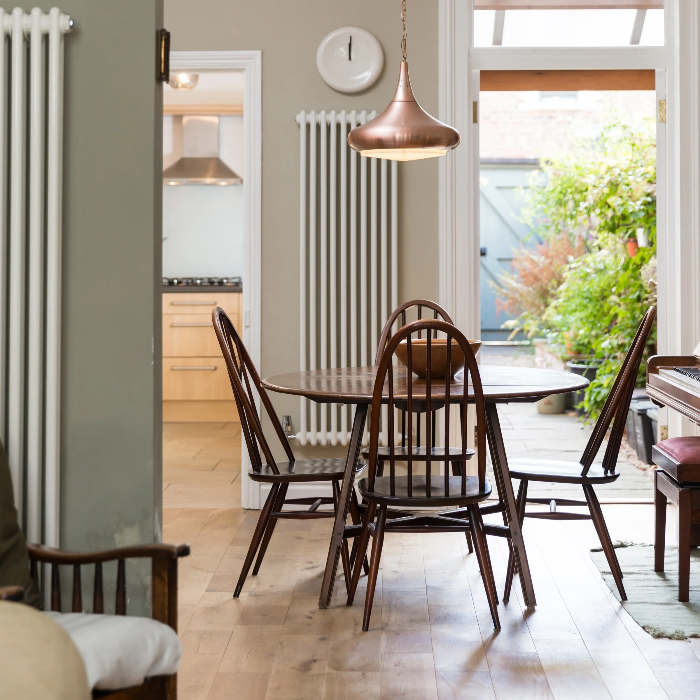four chair dining table with modern copper pendant light above and a open door showing a glimpse of the garden beyond