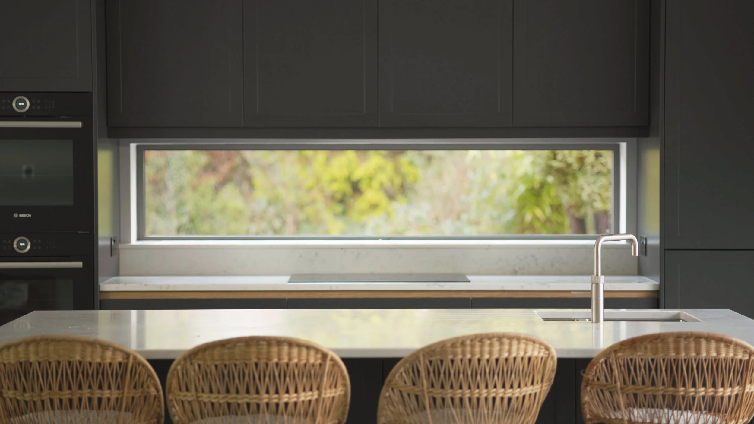 Empty, un-styled kitchen showing white quartz worktops, sink in the island and long panoramic splashback window above the worktop