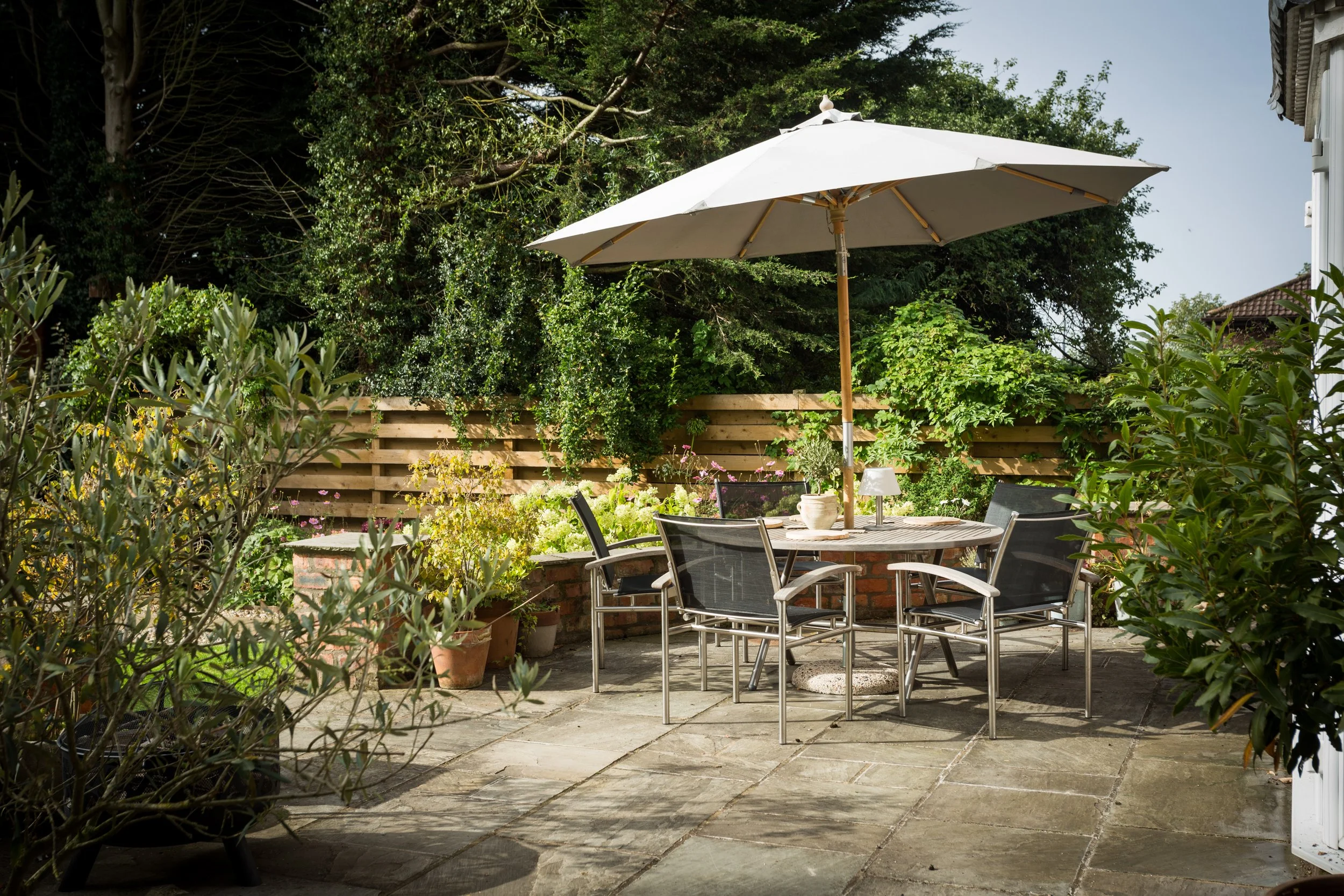 sunny patio area with small shrubbery, patio furniture and parasol