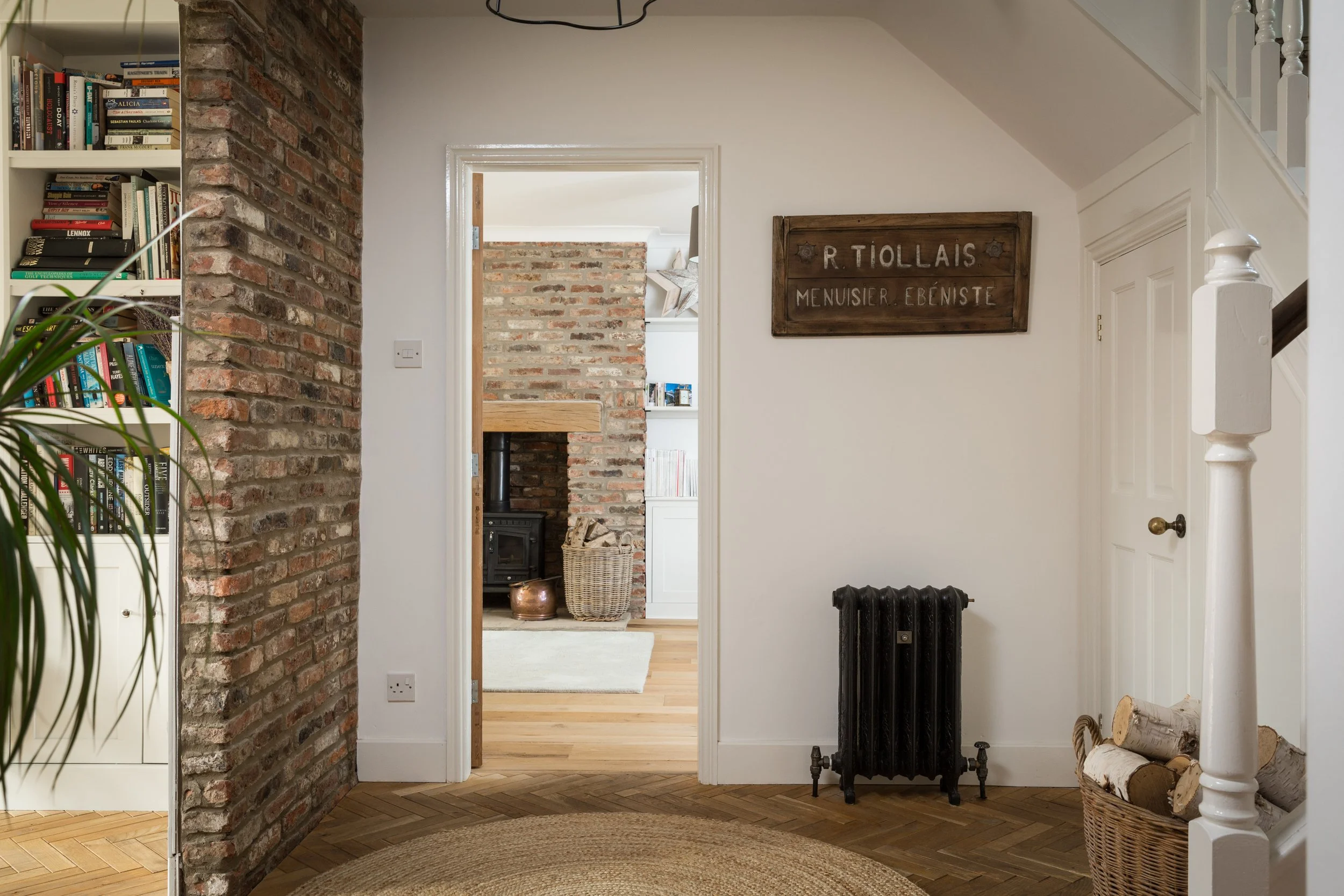one point perspective in entrance hall glimpsing into a room with fitted book shelving and into he kitchen with a brick surround fireplace with log burner