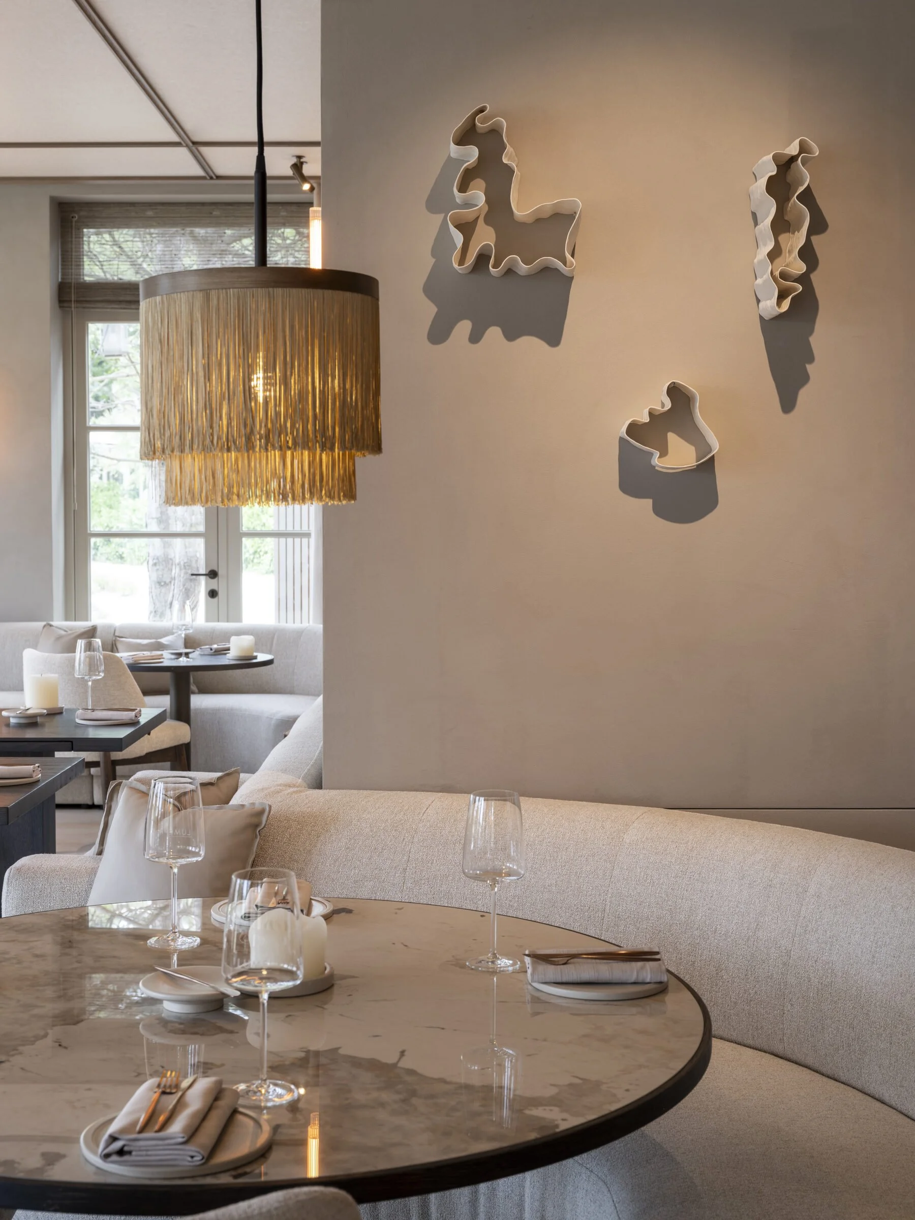 Curved banquette in the restaurant with wall sculptures and a fringed brass pendant