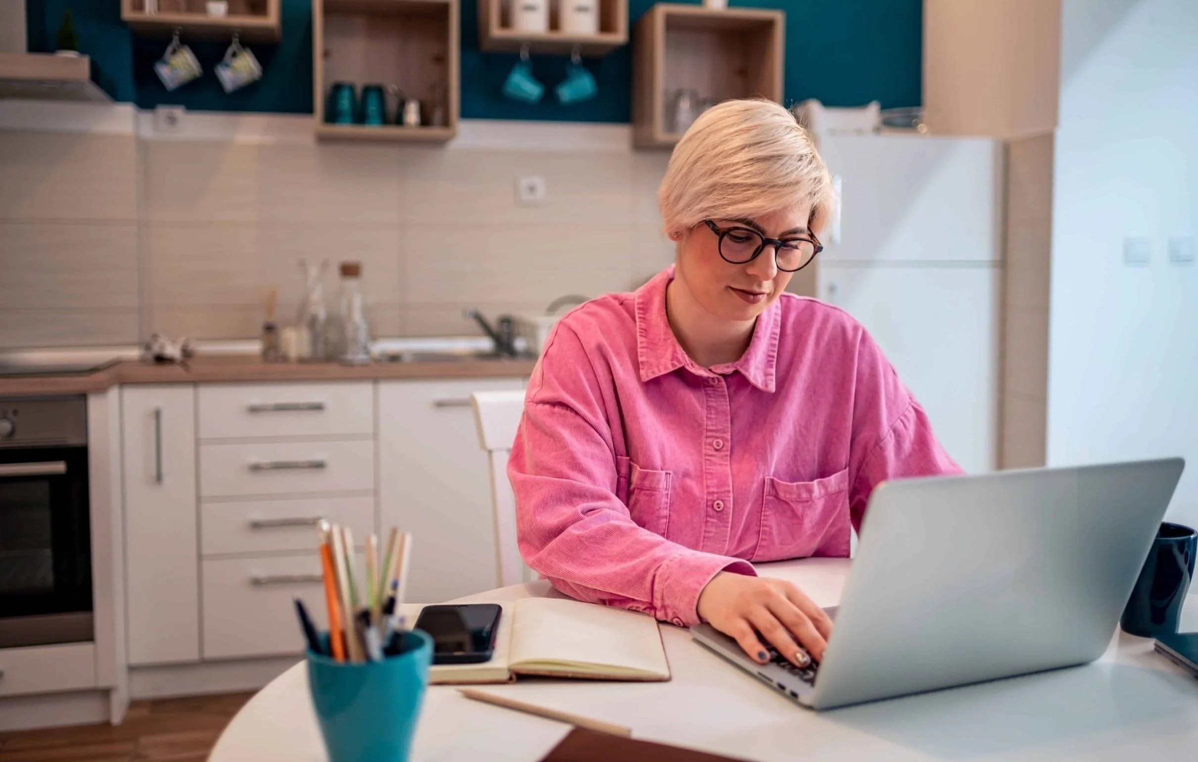 Person in pink shirt using a laptop in a kitchen setting.