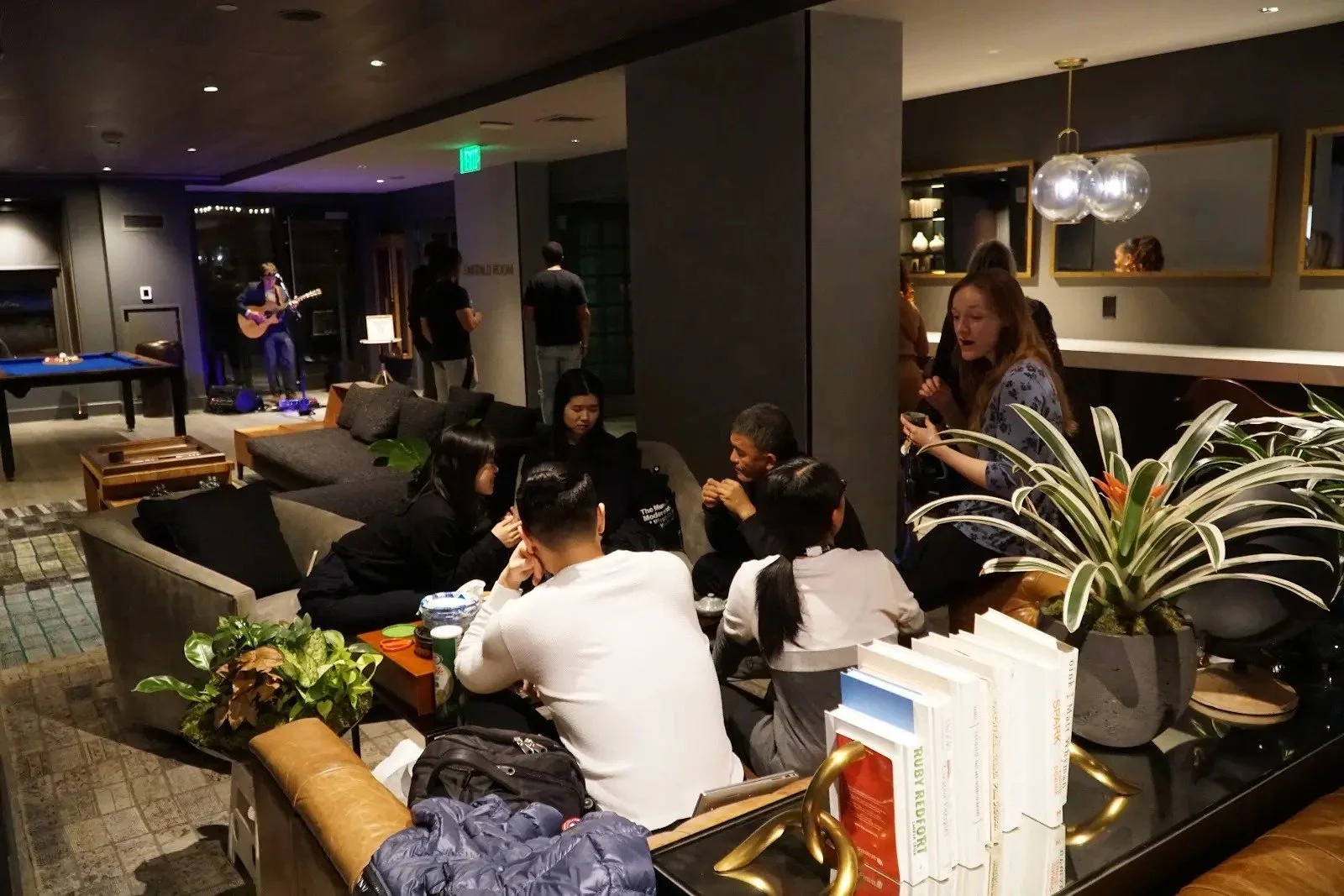 Guests talking in The Harlo residential lounge while a guitarist performs at a holiday event