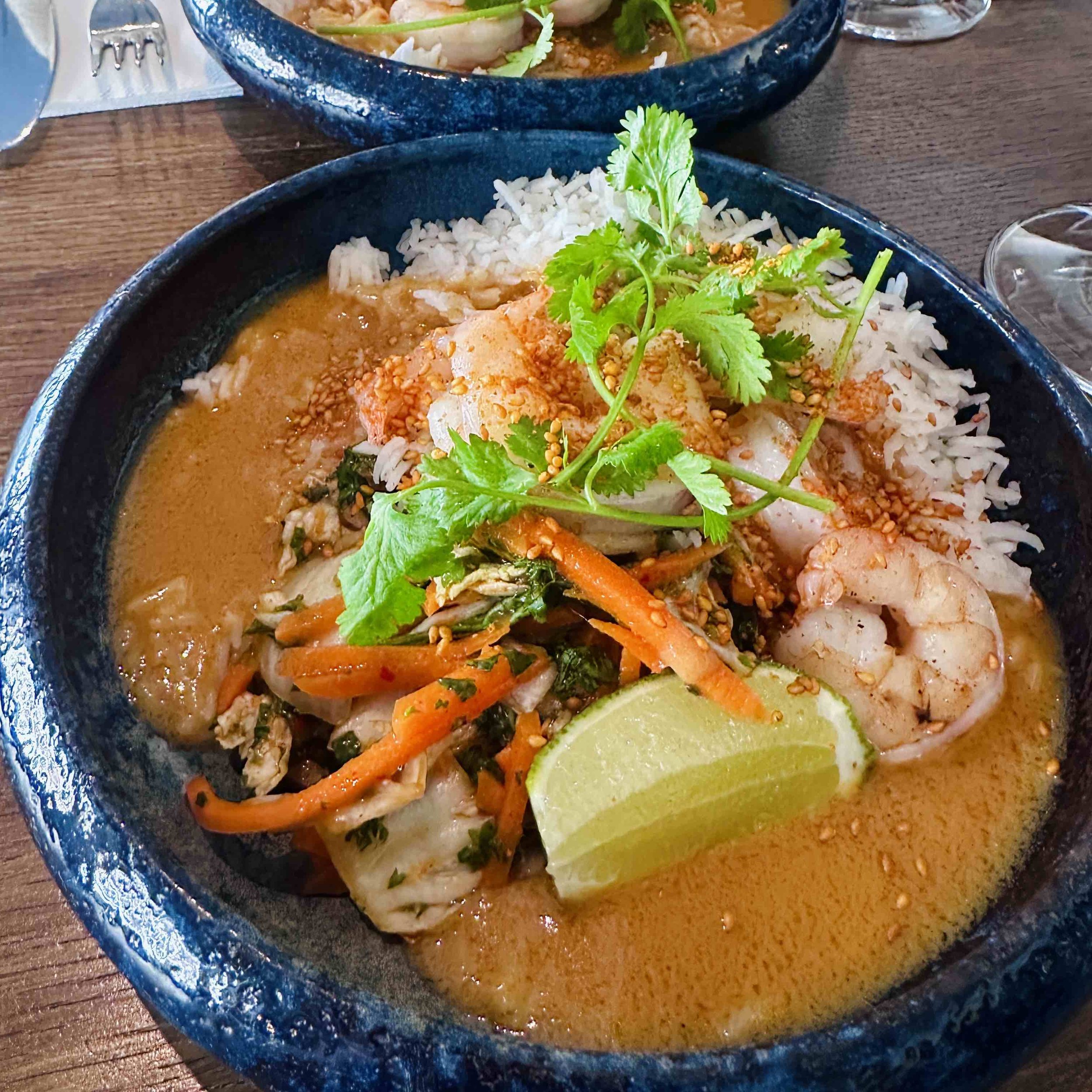 A blue bowl of coconut red curry with scampi, served with jasmine rice and topped with a mound of pickled shredded cabbage, carrots, and cilantro.