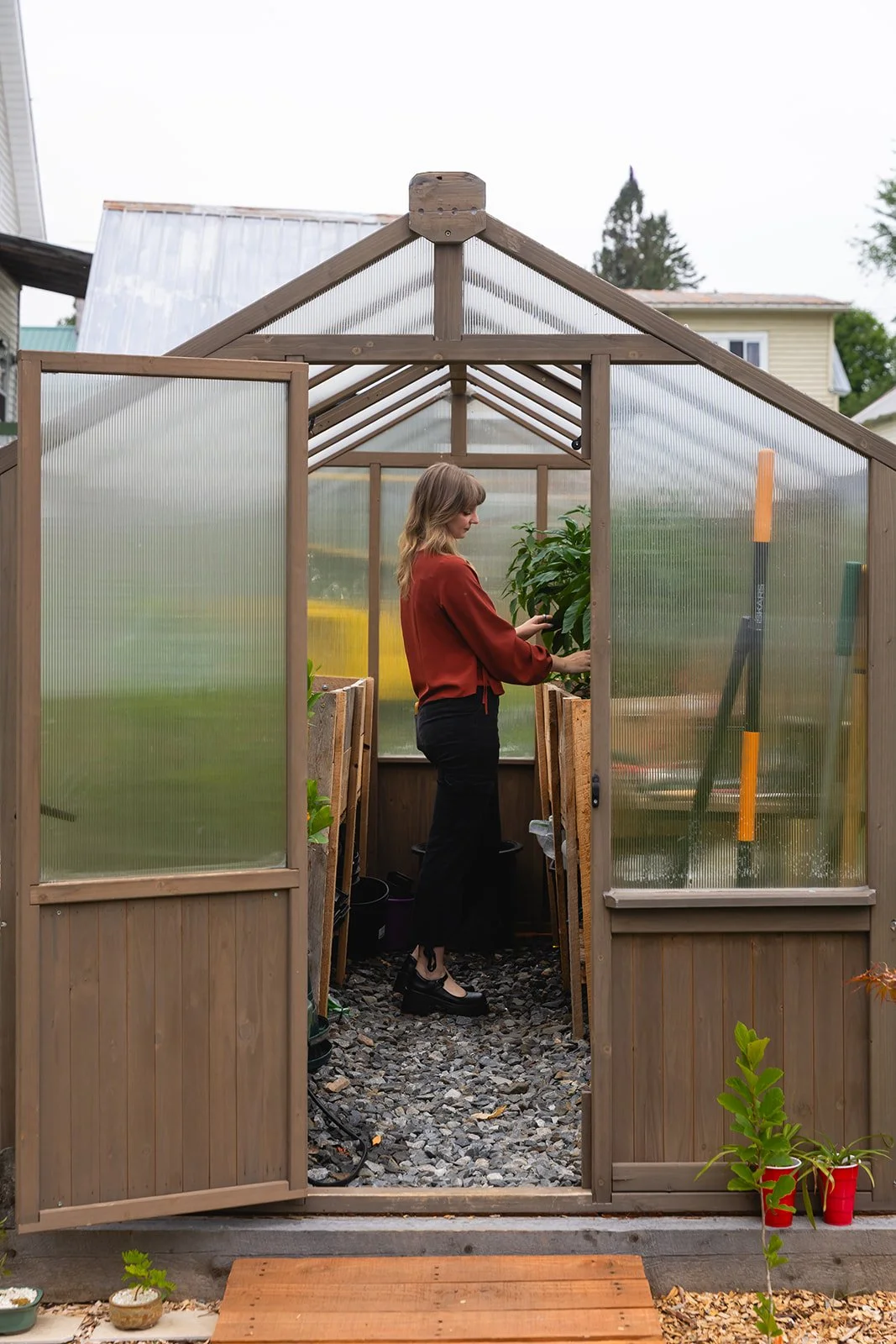 A woman standing inside a small greenhouse tending to a plant.