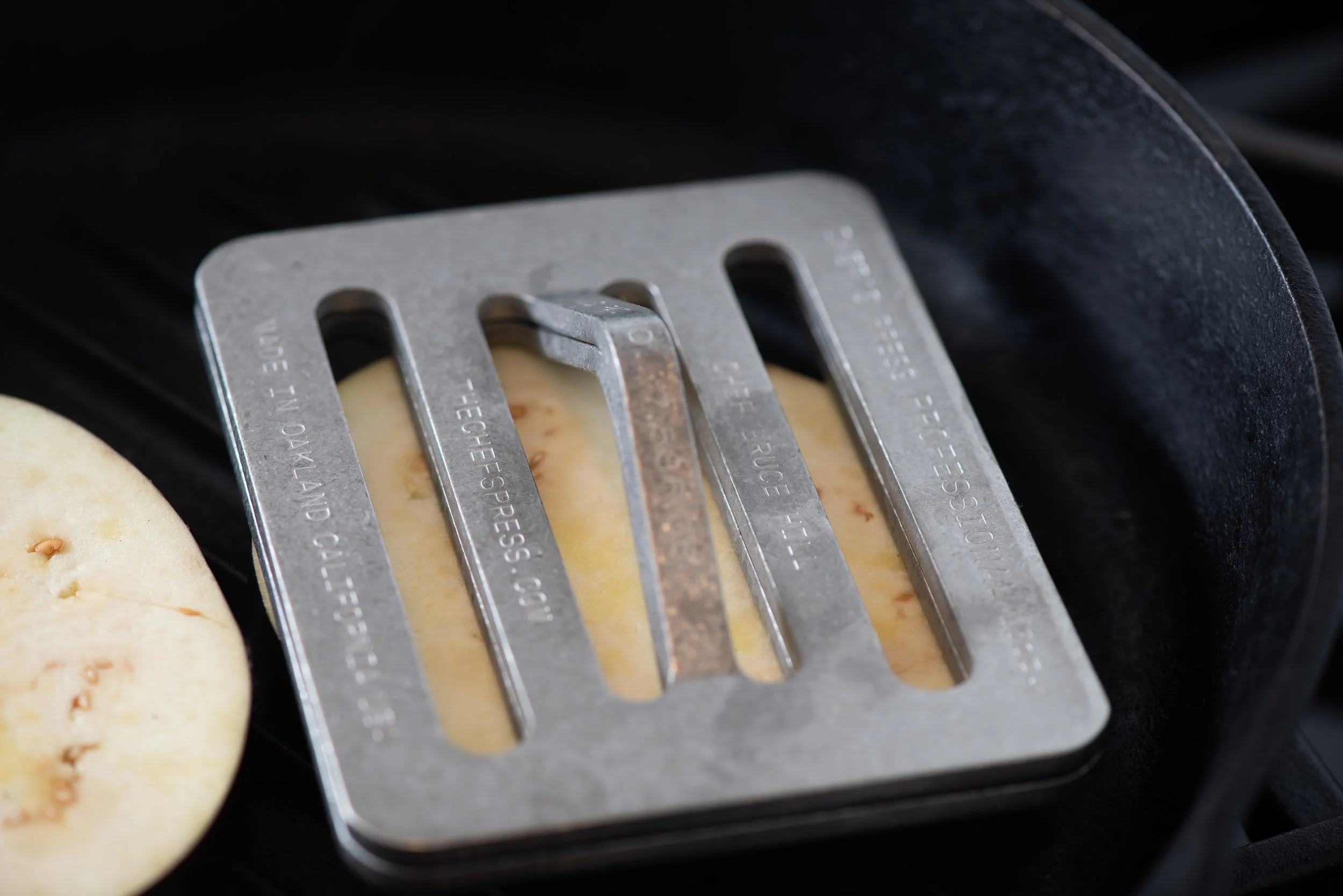 Close-up of a metal toast shredder on a black stovetop, with slices of bread underneath.