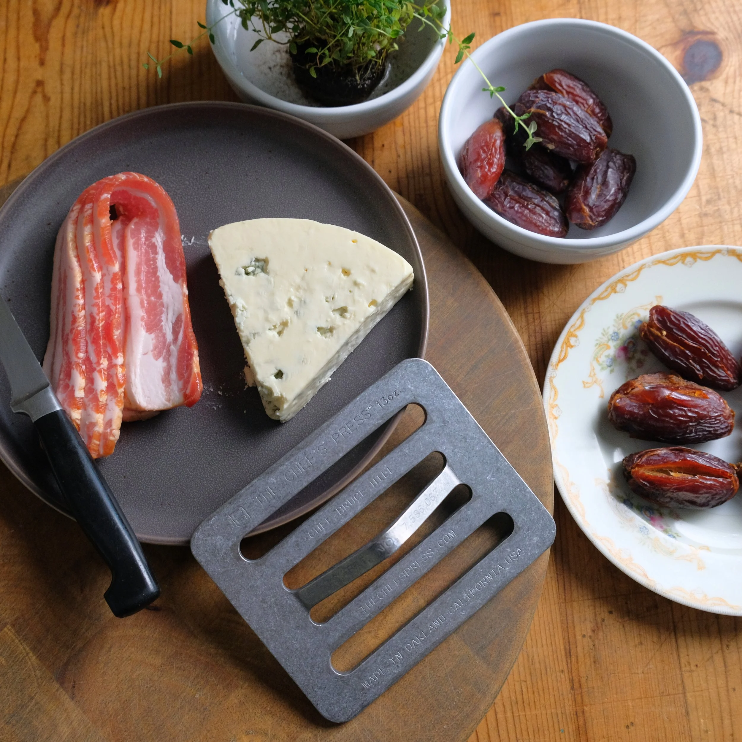 Assorted cheese, bacon, dates, and small bowls of dried fruit on a wooden table.