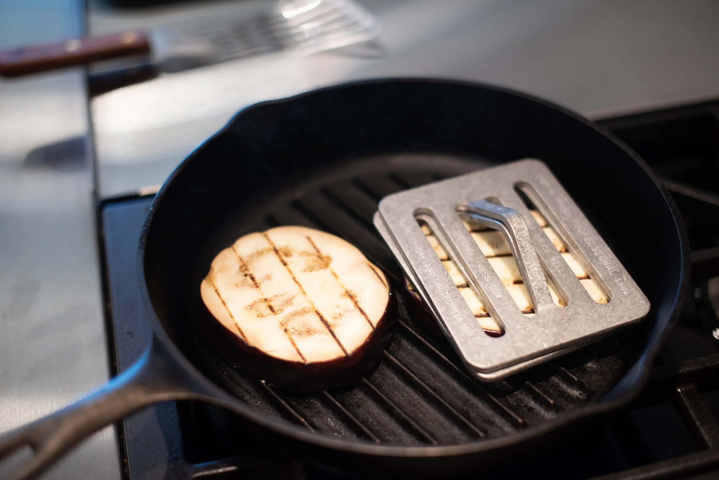 A cast iron skillet with a grilled slice of sweet potato on a stovetop, with grill marks on the sweet potato slice.