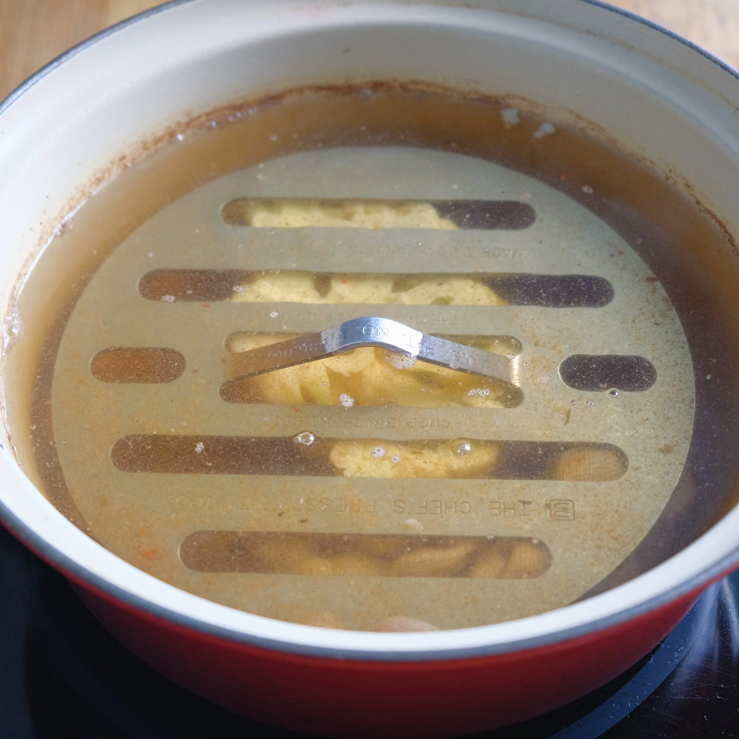 A pot with a metal steaming rack inside, filled with boiling water and partially cooked chicken.