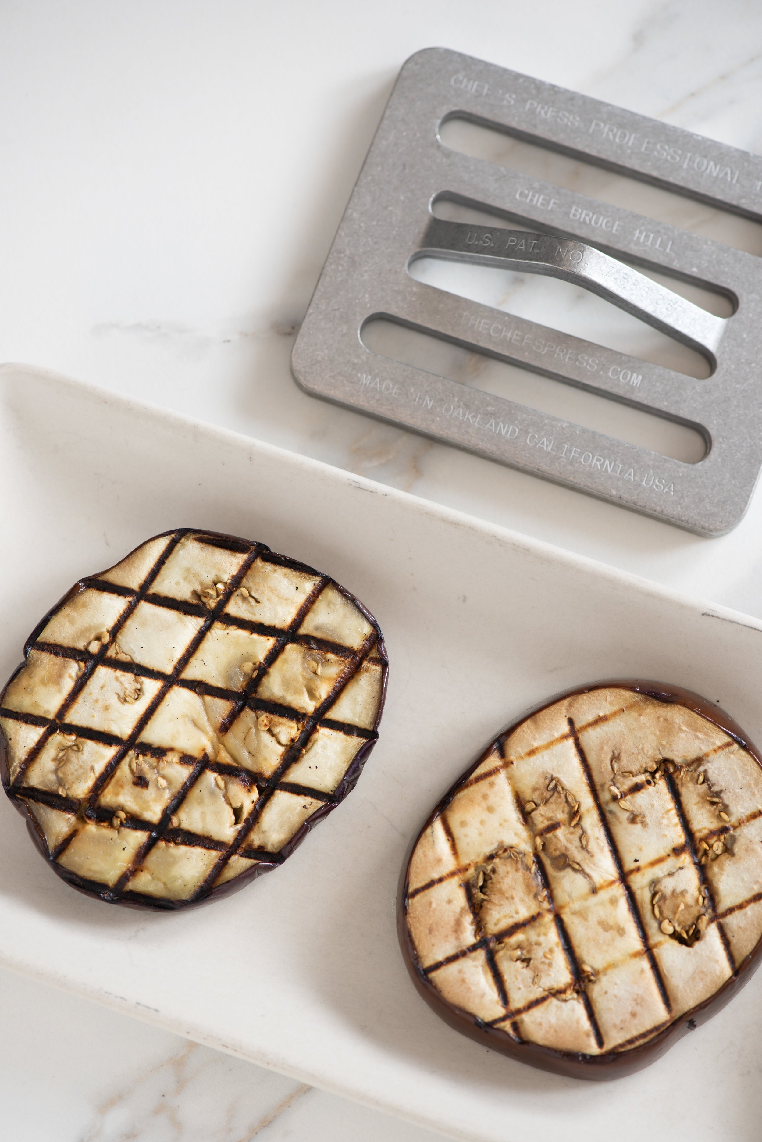 Two round mini cheesecakes topped with chocolate drizzle and nuts, placed on a white rectangular dish.