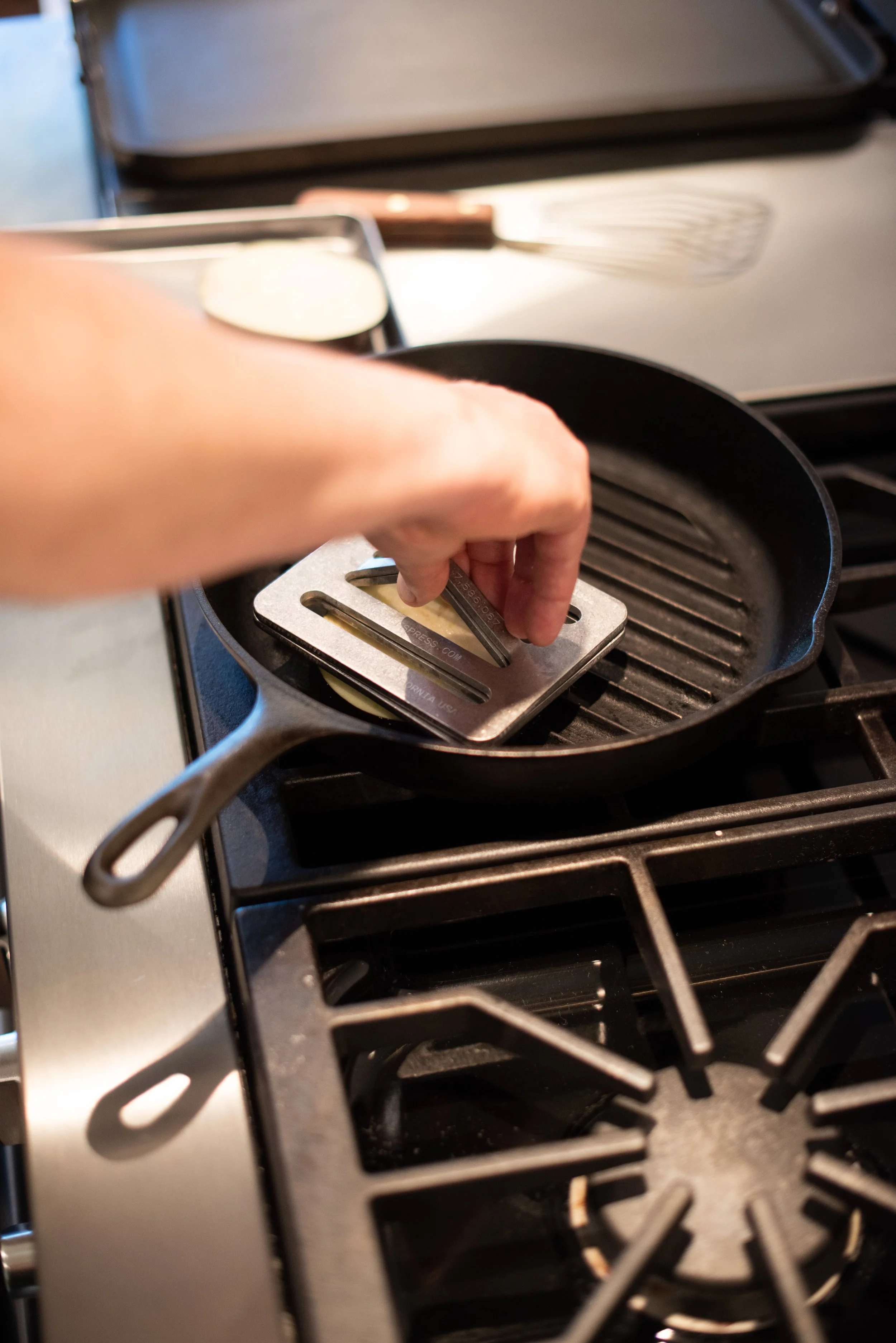 A person placing a metal stovetop pressure cooker into a cast-iron grill pan on a stove.