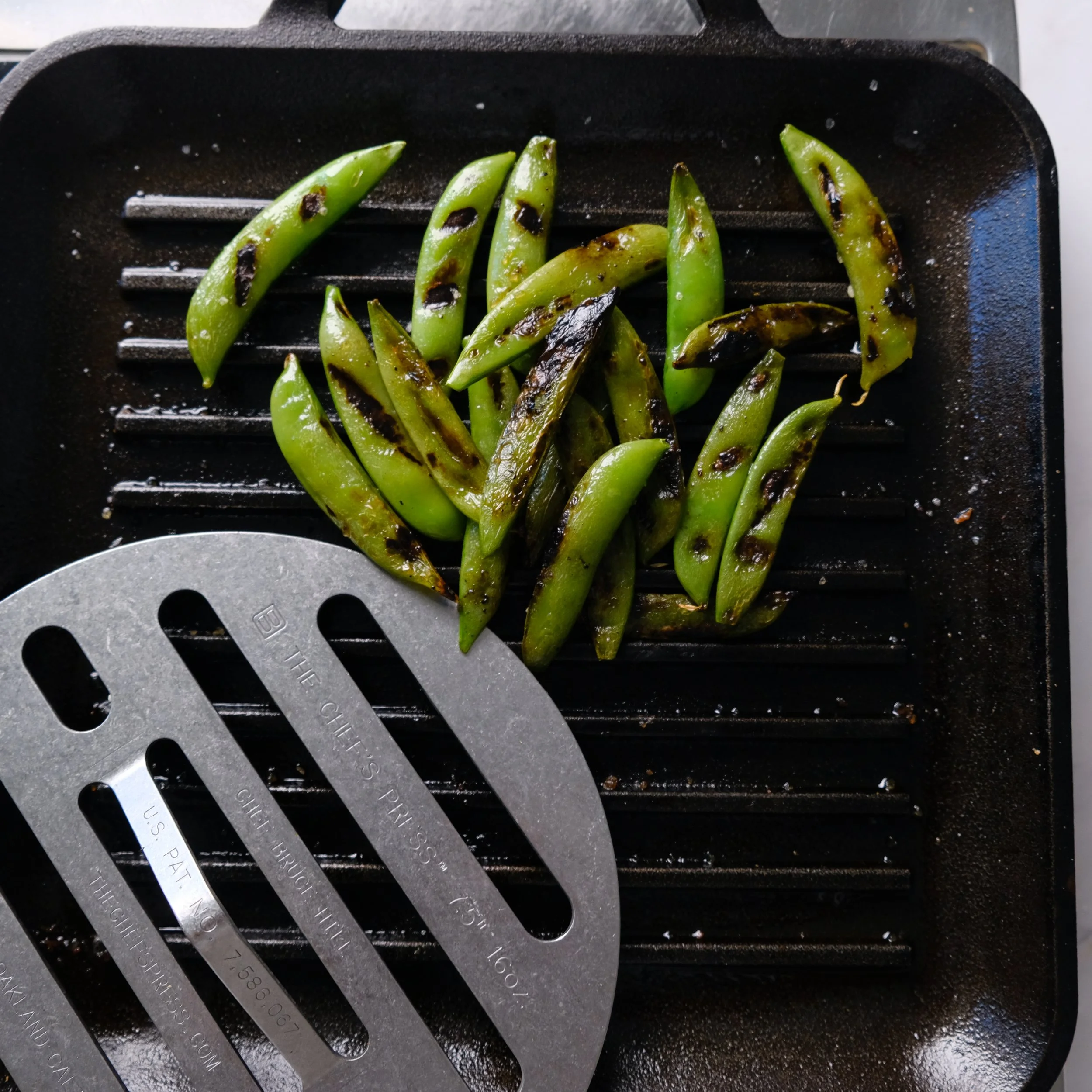 Grilled snap peas on a grill pan with a metal spatula.