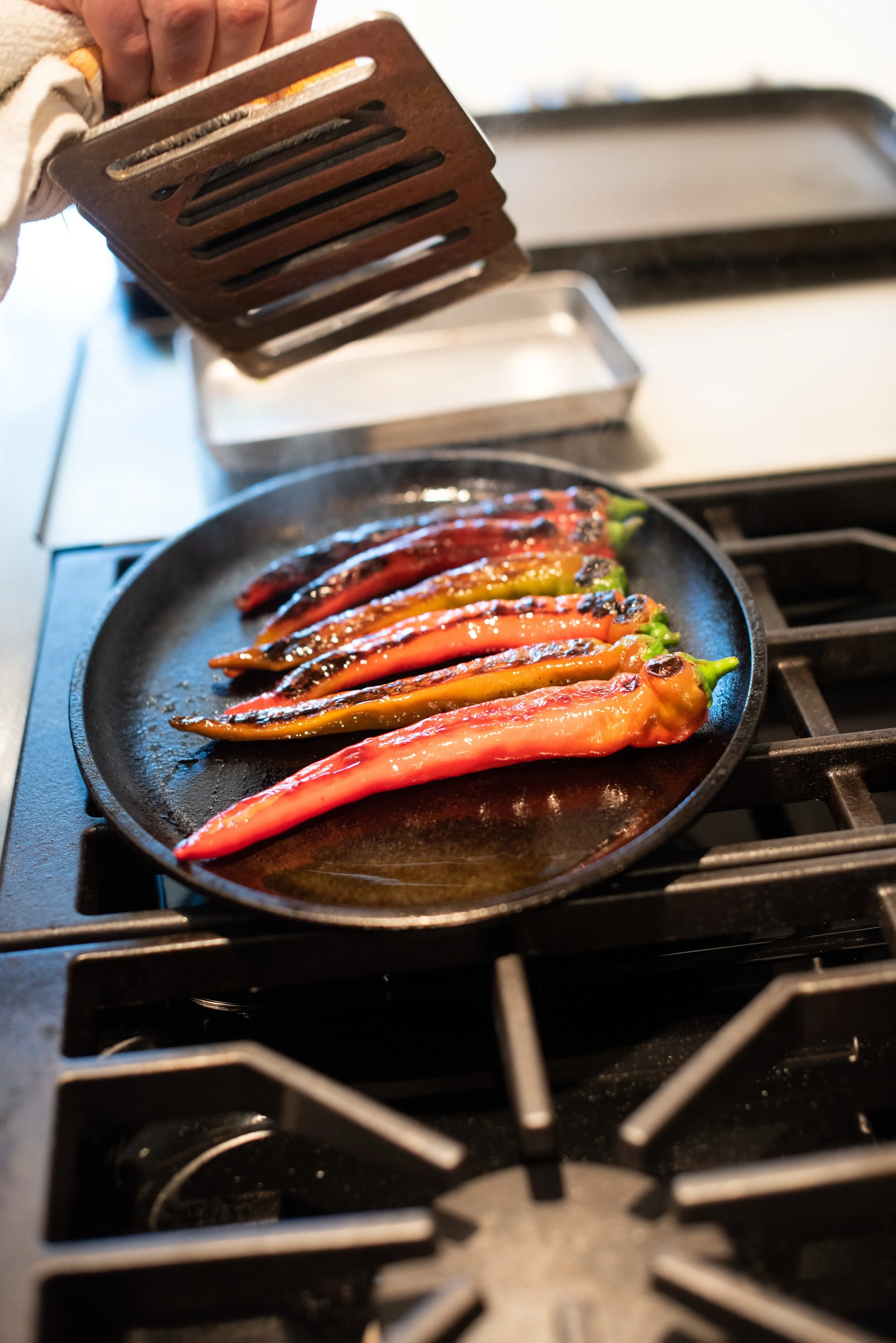 Colorful chili peppers being roasted in a black cast iron skillet on a stovetop.