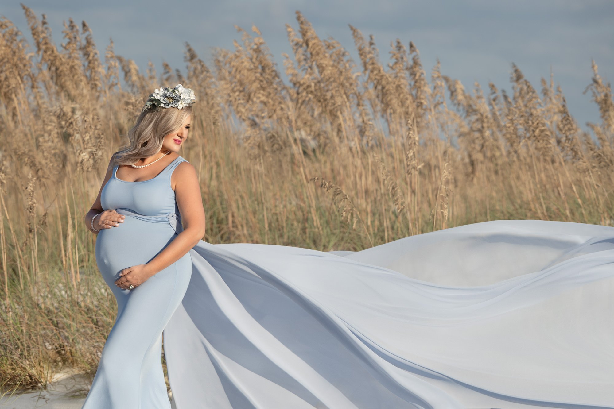 Pregnant woman in a flowing blue dress with floral crown standing in a field.
