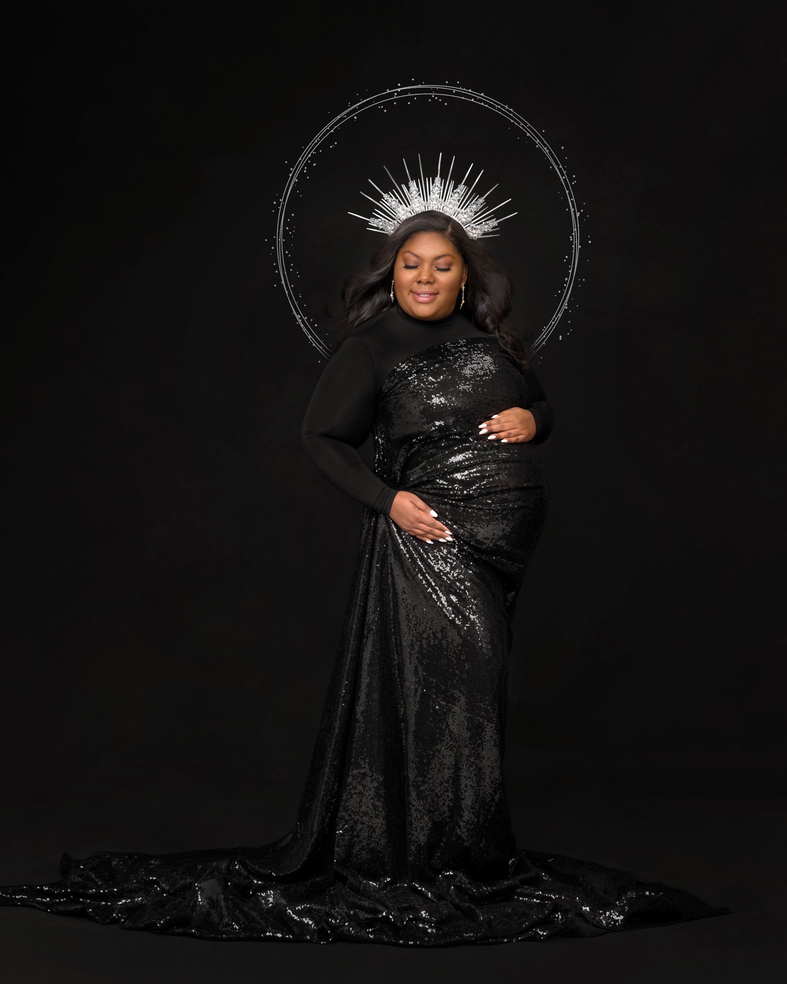 Pregnant woman in elegant black sequin gown with silver headpiece and halo effect on a black background.