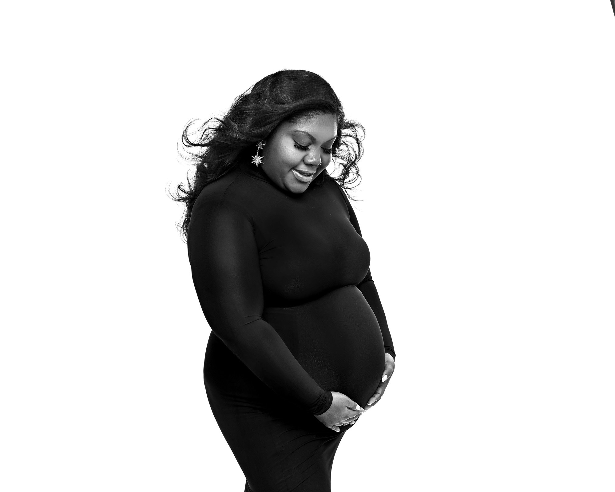 Pregnant woman in black dress holding her belly, smiling, with flowing hair, isolated on white background.