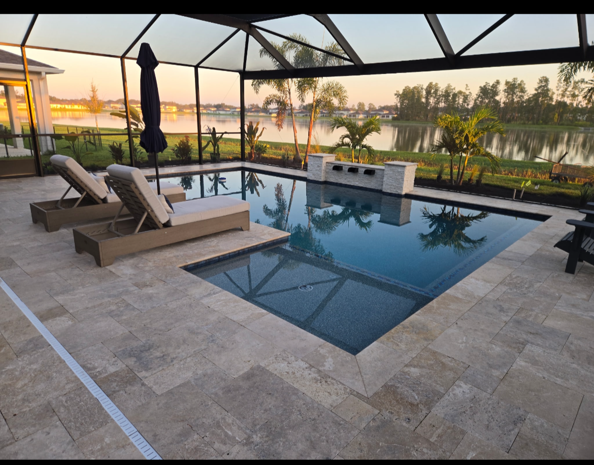 Screened backyard pool area with two lounge chairs, an umbrella, and a view of a lake with palm trees at sunset.