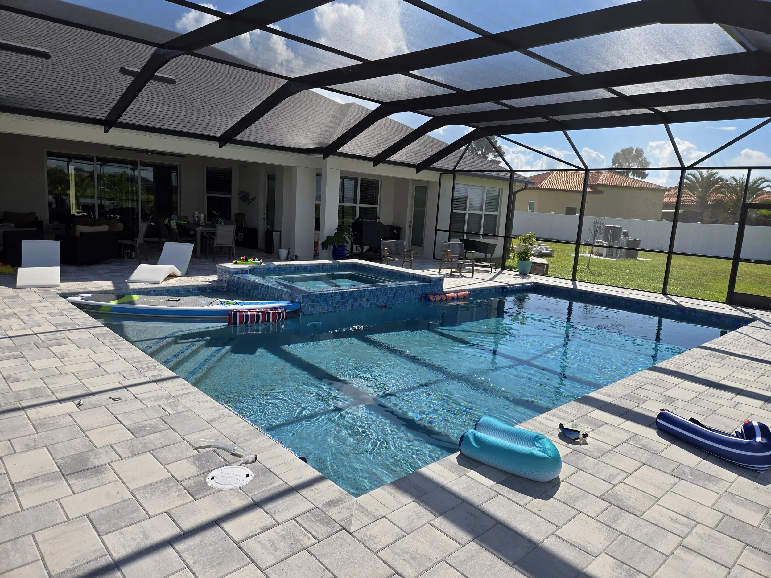 Backyard enclosed pool area with patio furniture, a hot tub, and swim floats under a screen enclosure.