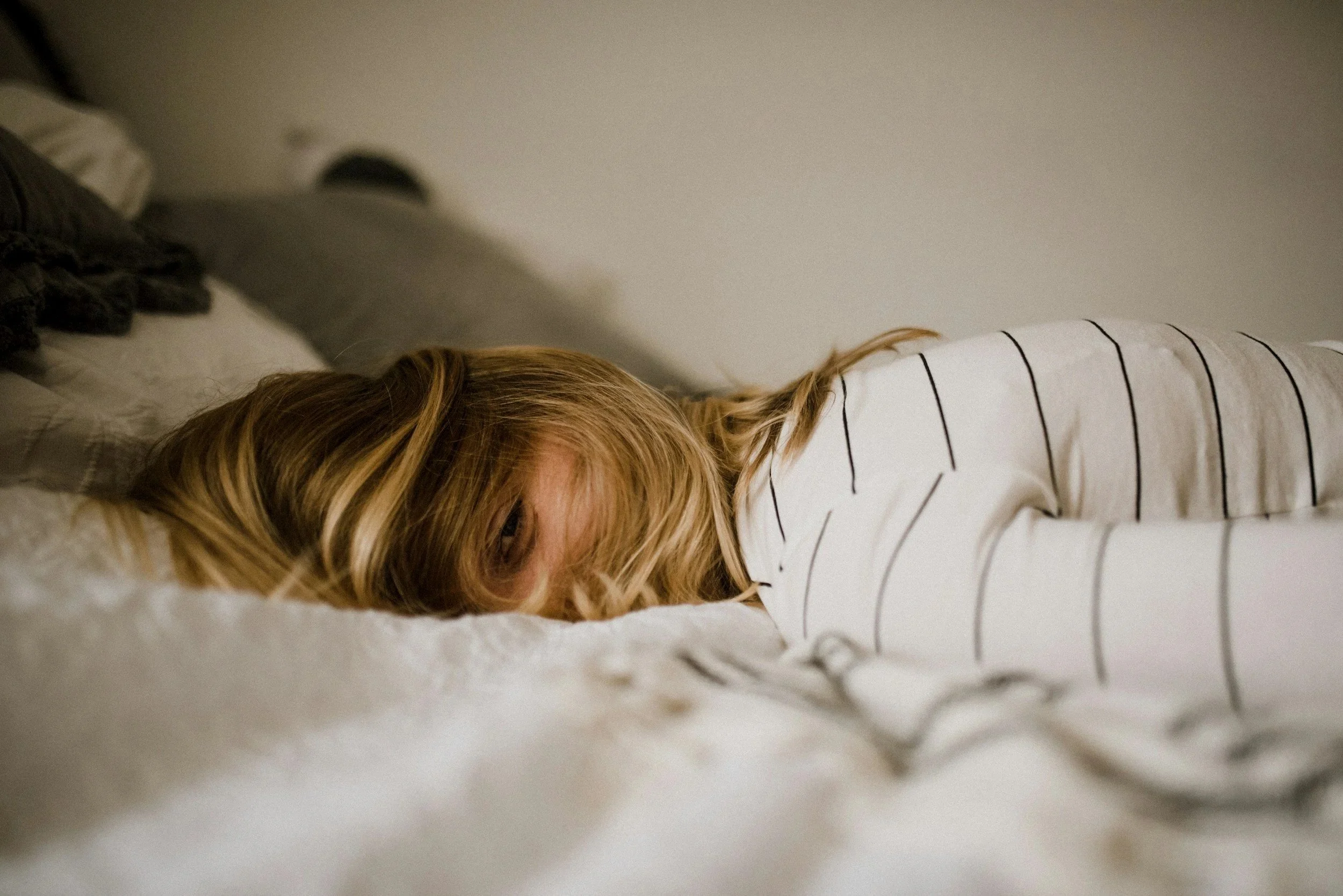 Woman laying face down on the bed hair covering her entire face with one eye showing. Treating hashimotos naturally is on her mind.