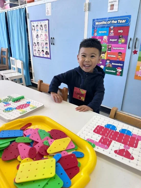 A smiling UMC Preschool student playing at a classroom table