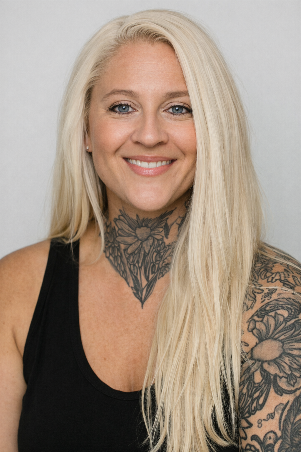 Close-up portrait of a young woman with curly hair smiling, wearing a black tank top and a gold necklace.