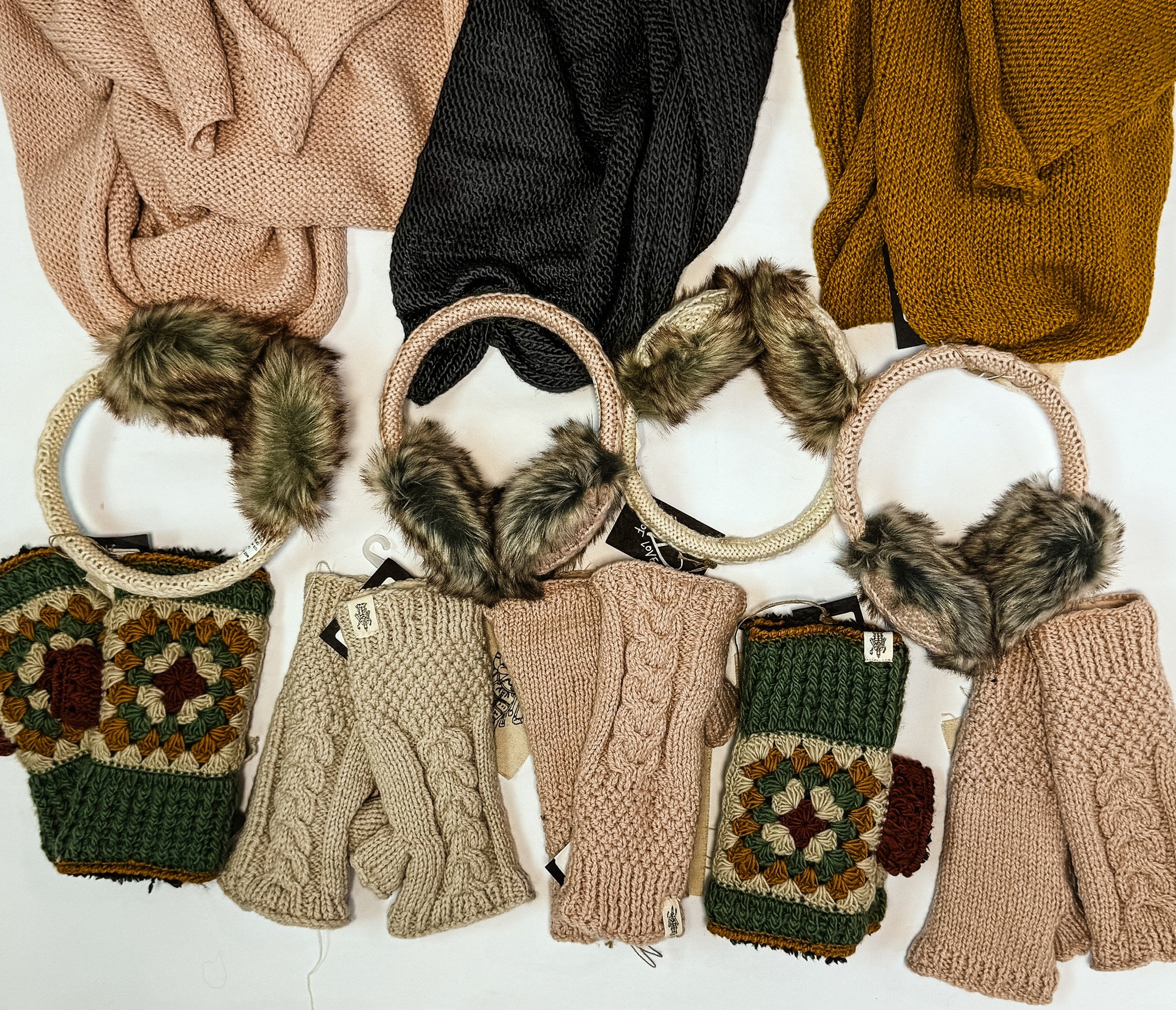 A collection of knitted winter accessories including scarves, mittens, and headbands, with some featuring faux fur pom-poms, in various colors and patterns.