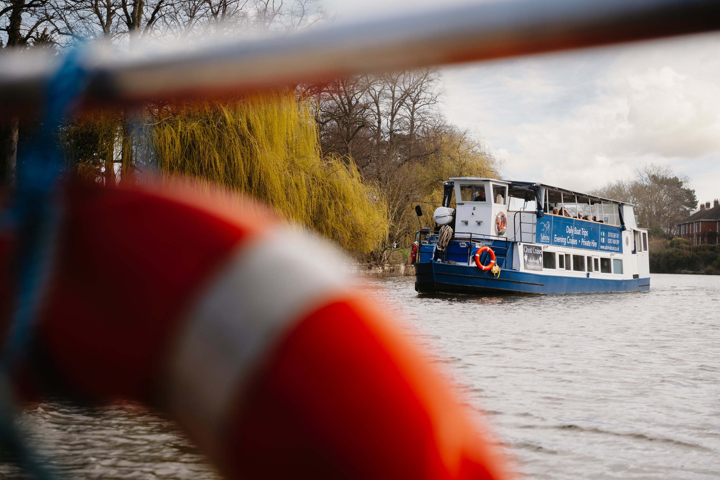 The Sabrina Boat carrying passengers along the River Severn in Shrewsbury, with the open green space of Shrewsbury Quarry visible in the background in Shropshire.