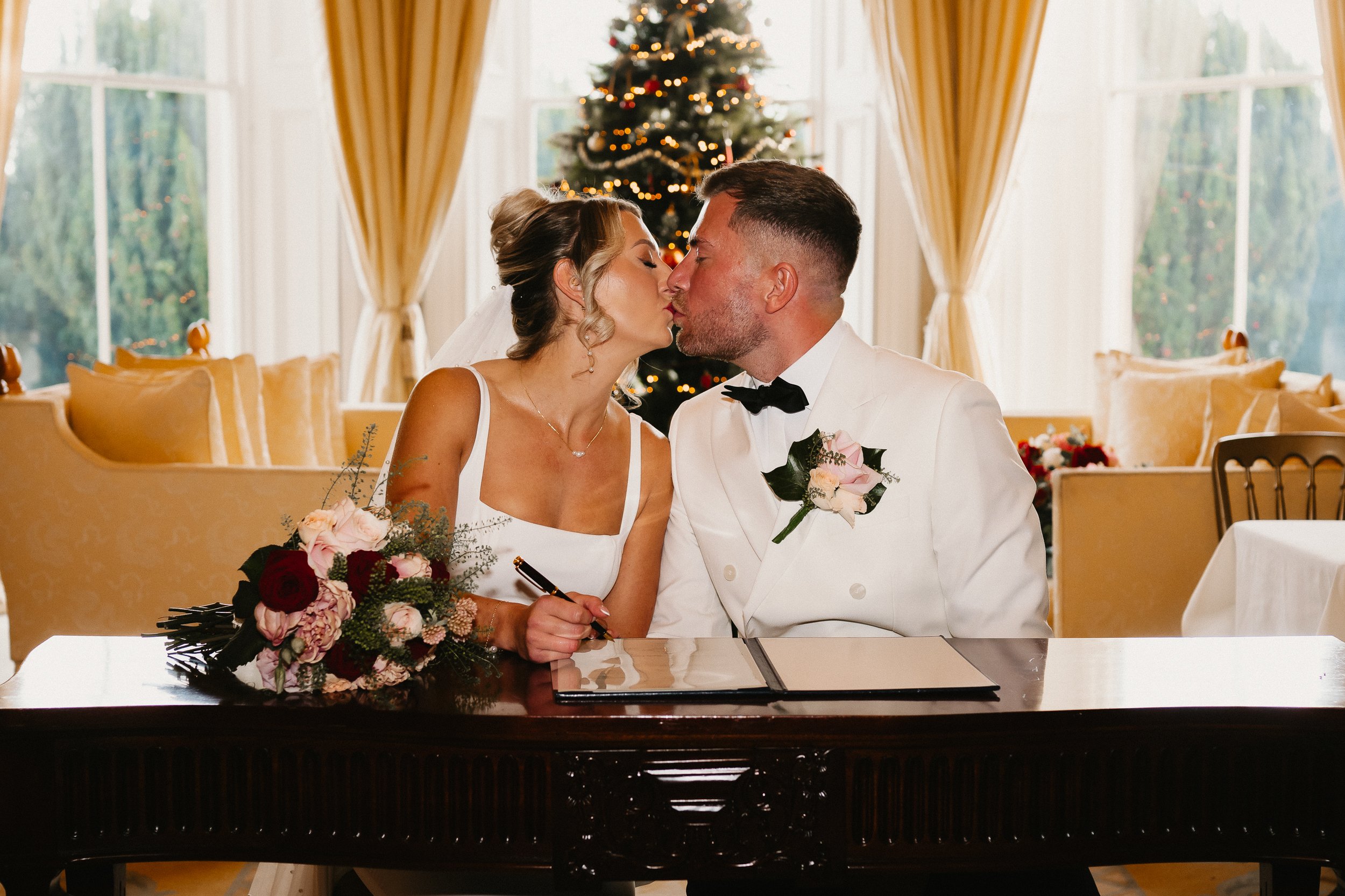 Bride and groom signing the wedding register during their winter ceremony at Netley Hall, seated at a decorated table inside the venue.