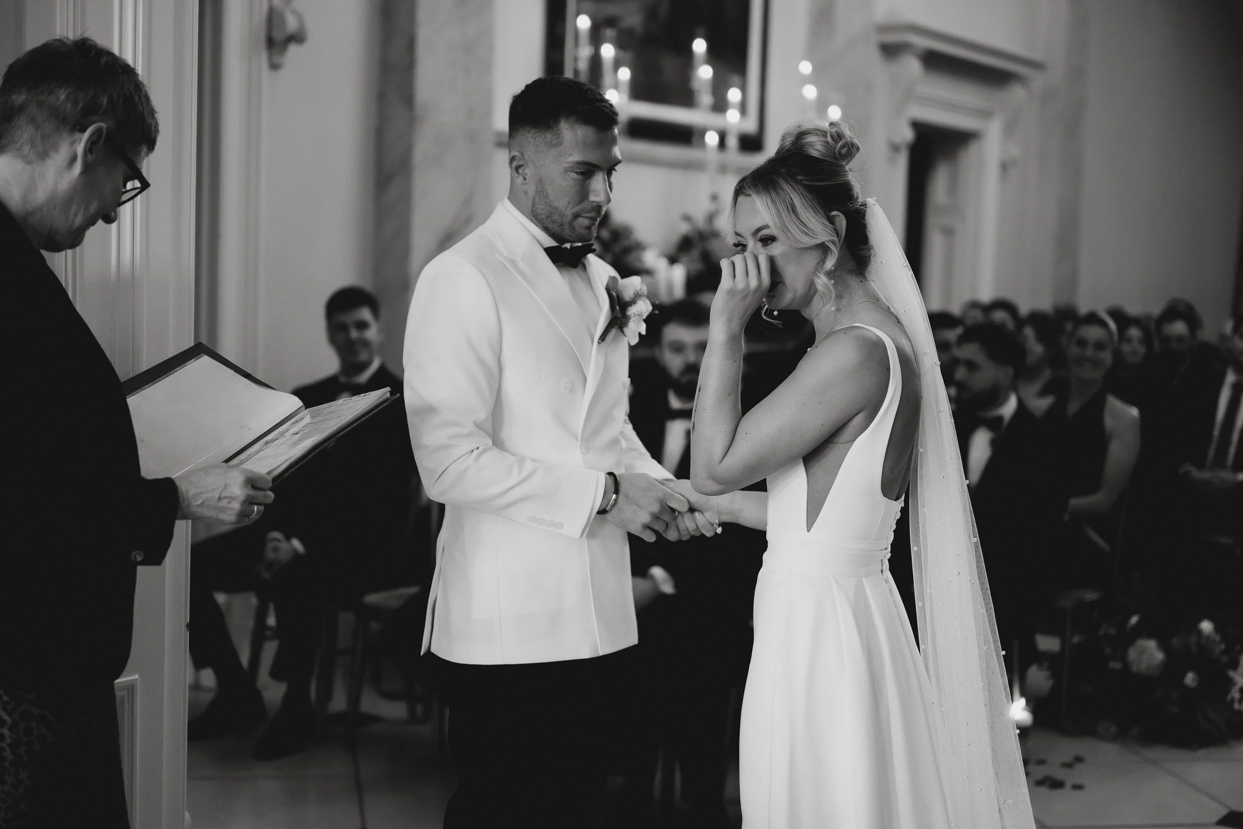 Bride and groom during their winter wedding ceremony inside Netley Hall in Shropshire, with guests seated around them.