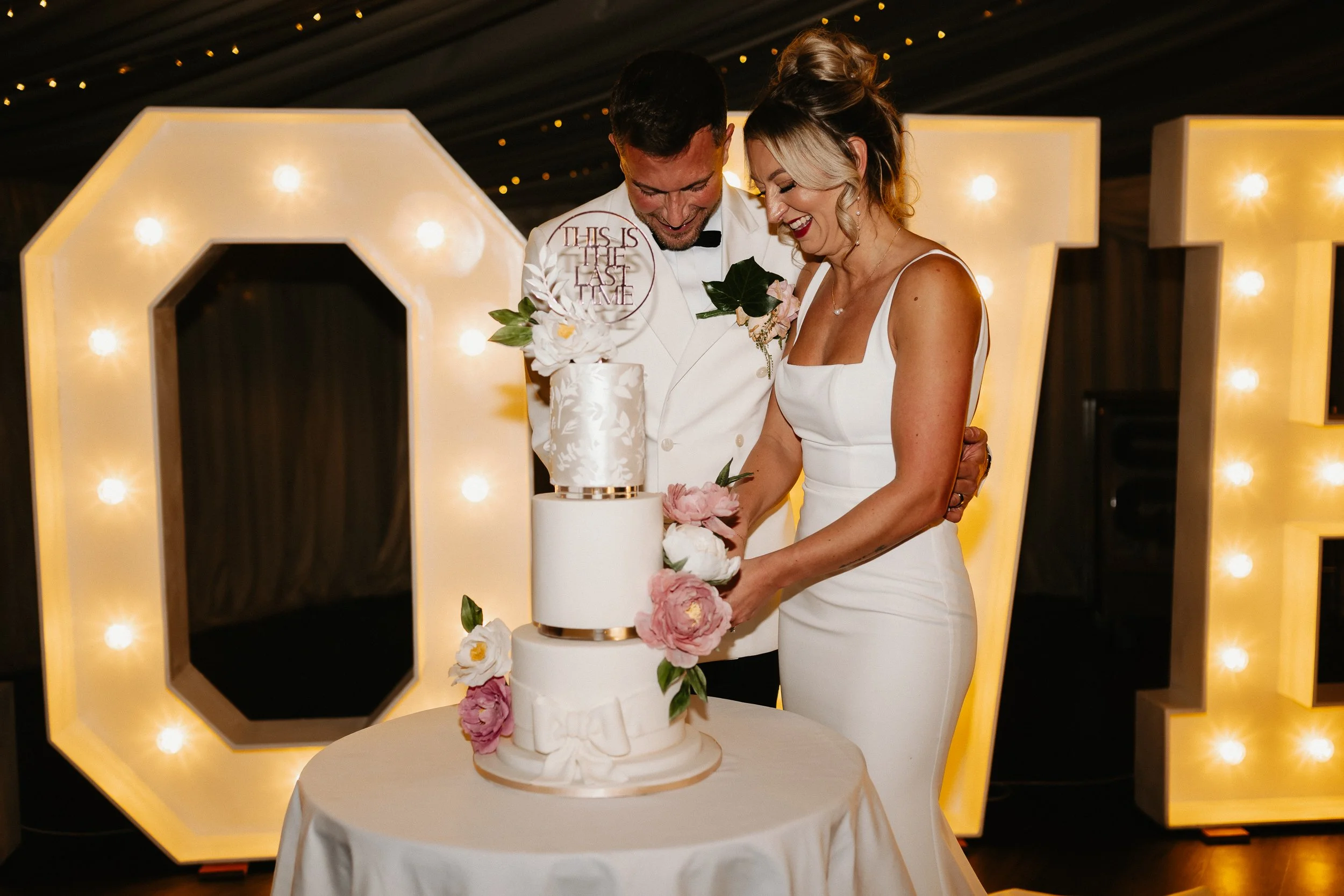 Bride and groom cutting their wedding cake during the winter reception at Netley Hall, surrounded by cheering guests.