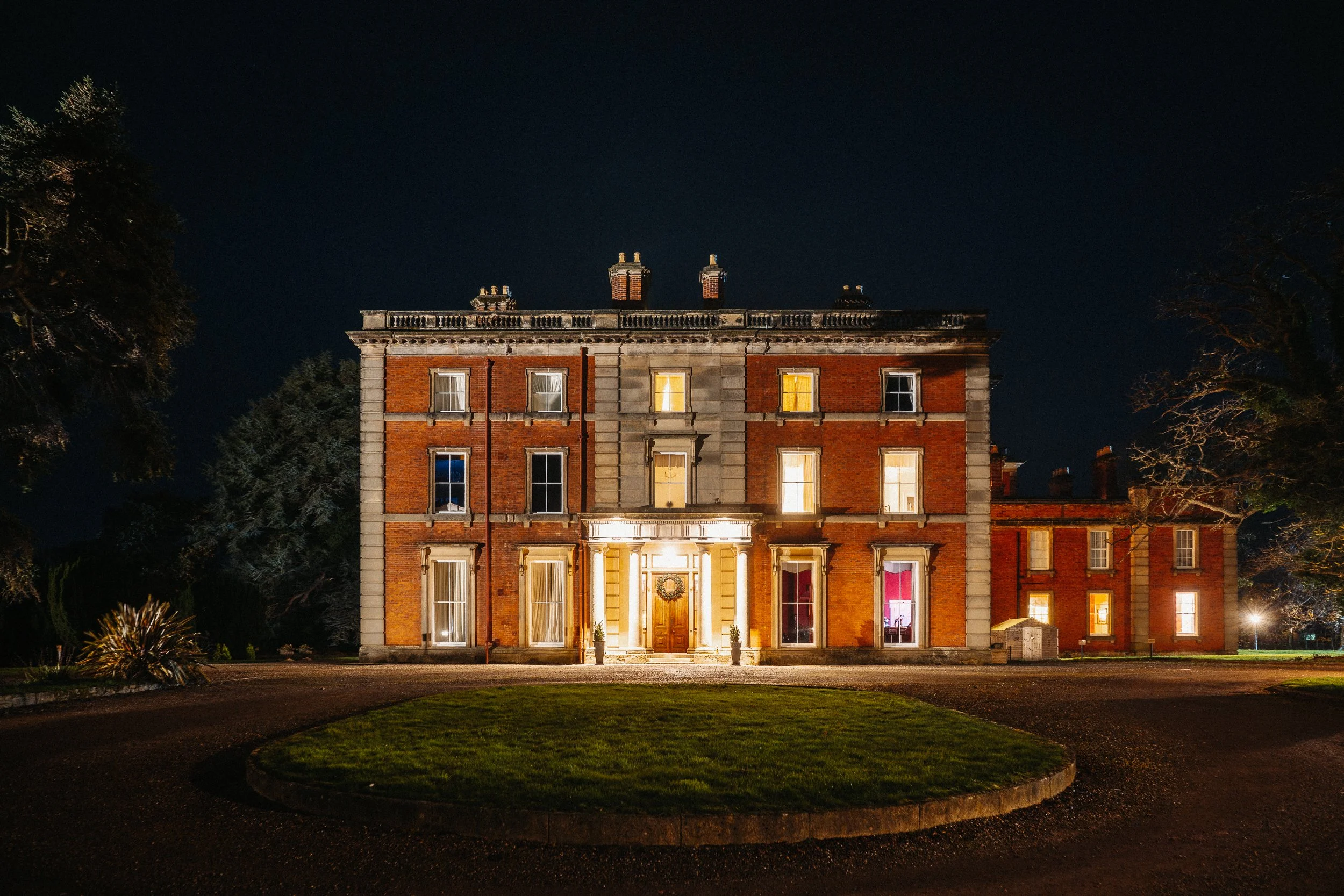 Exterior of Netley Hall lit up at night during a winter wedding, with warm lights glowing against the dark sky.