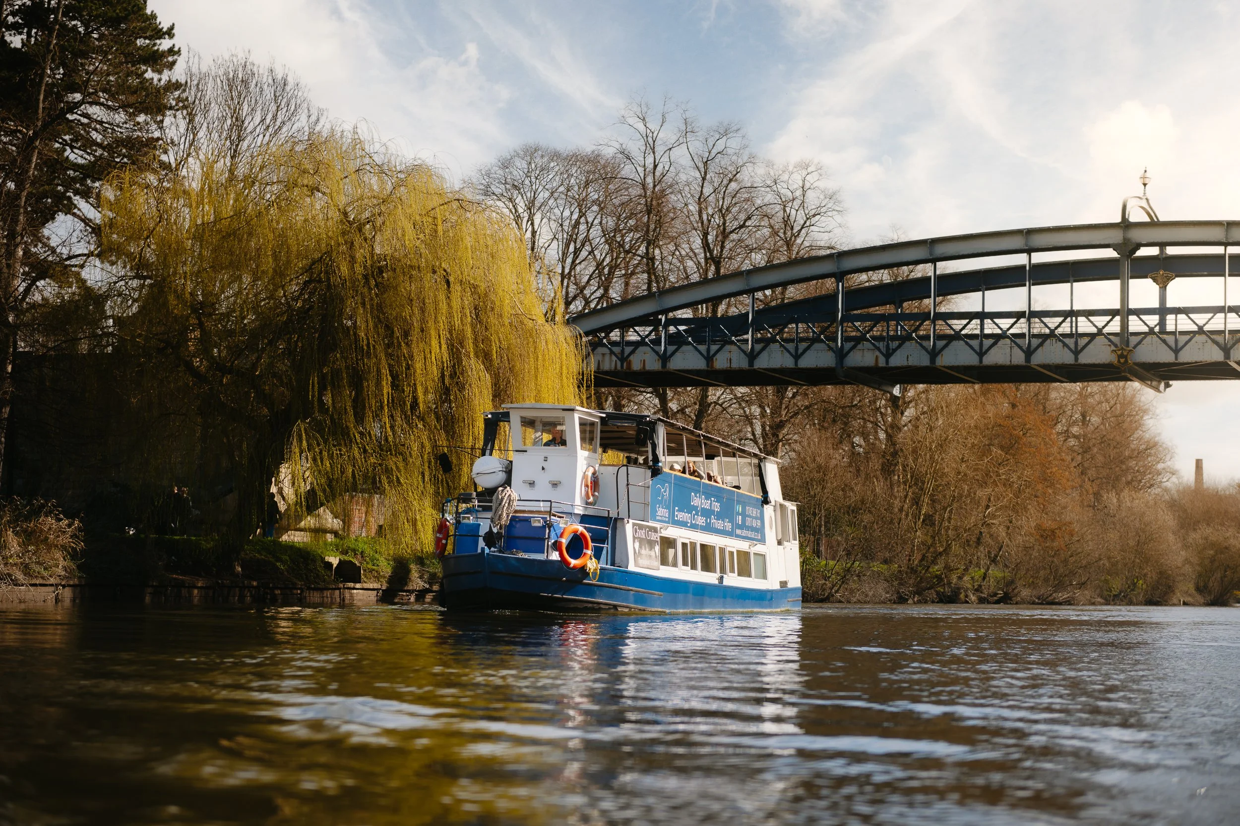The Sabrina Boat carrying passengers along the River Severn in Shrewsbury, with the open green space of Shrewsbury Quarry visible in the background in Shropshire.