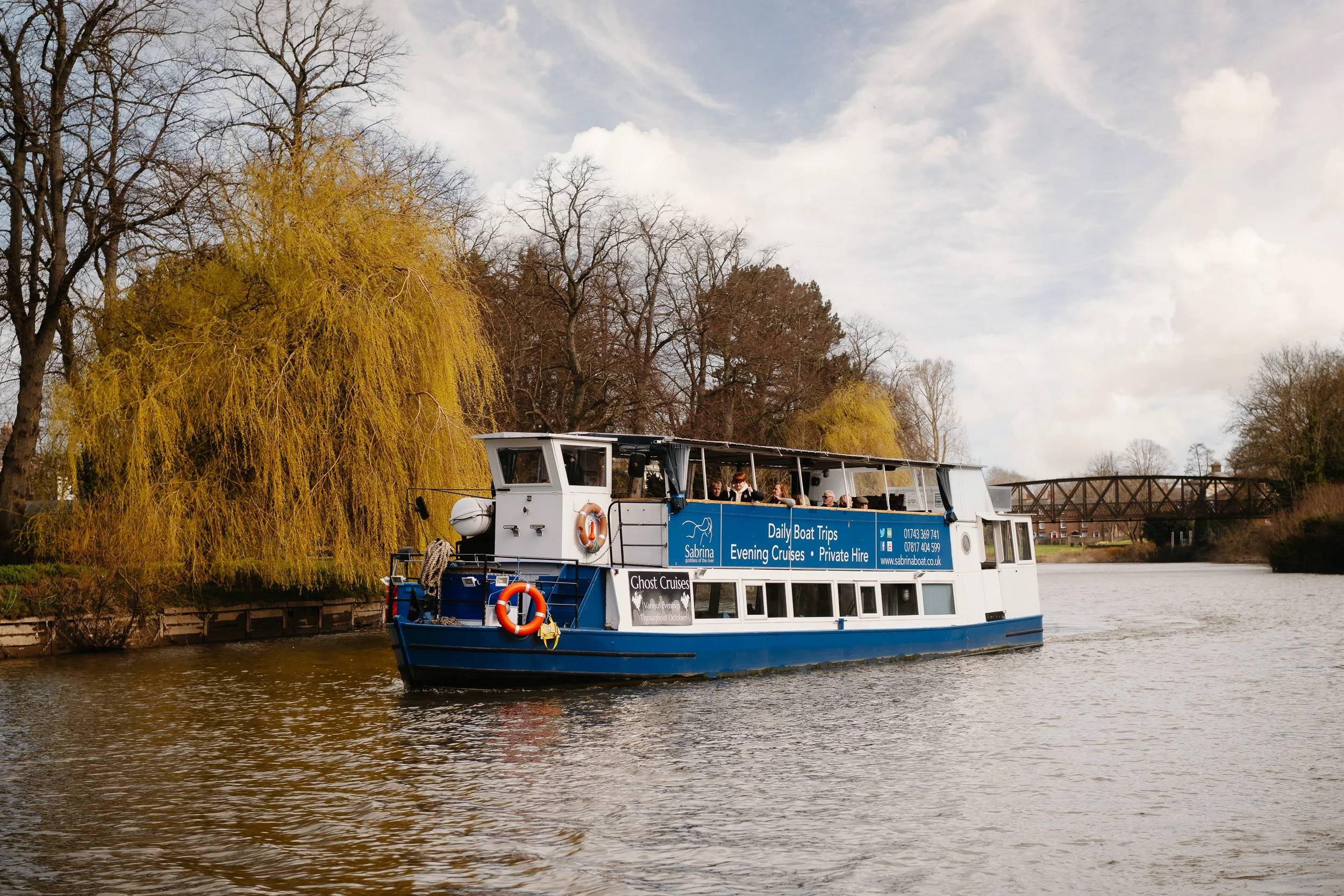 The Sabrina Boat carrying passengers along the River Severn in Shrewsbury, with the open green space of Shrewsbury Quarry visible in the background in Shropshire.