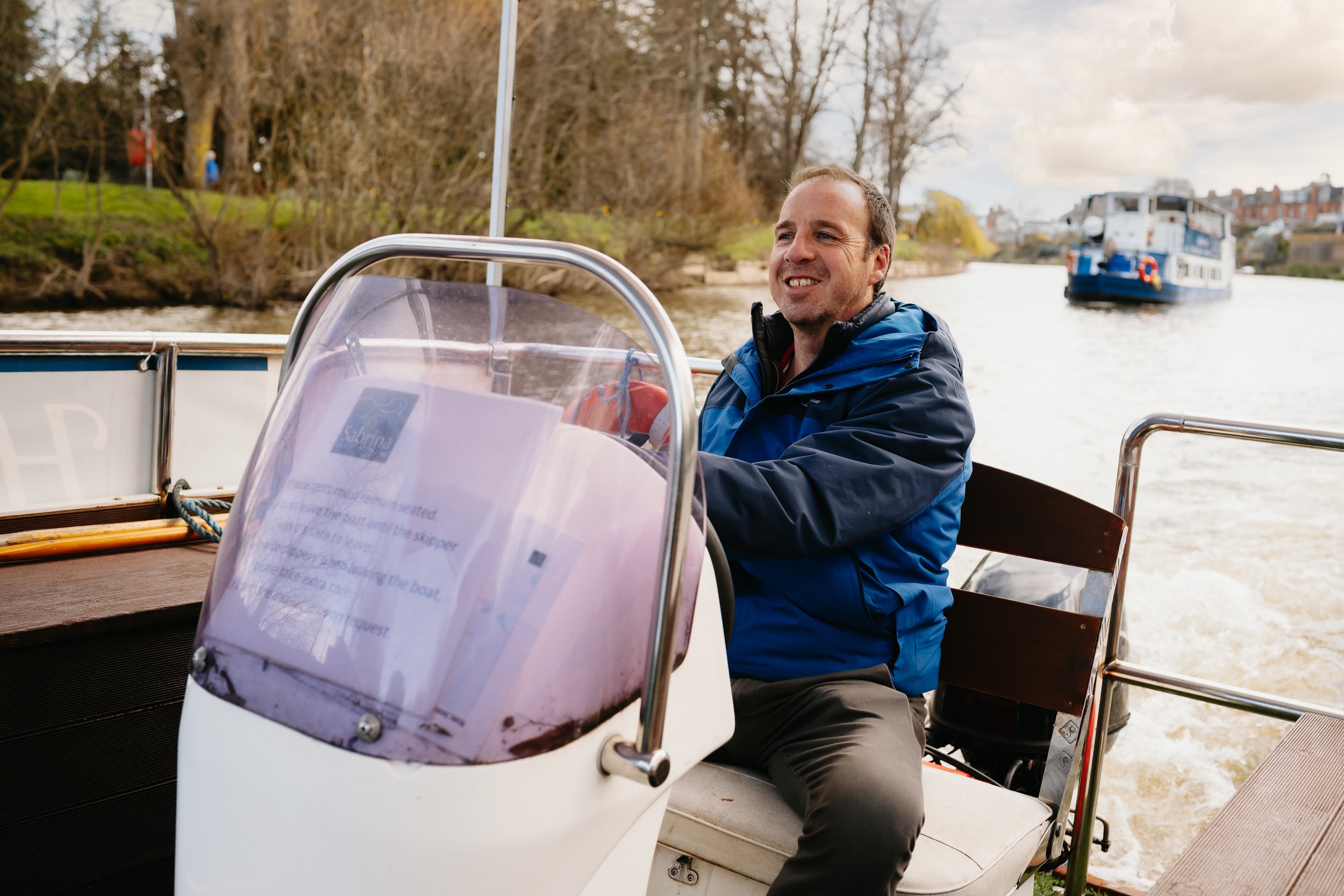 The Sabrina Boat carrying passengers along the River Severn in Shrewsbury, with the open green space of Shrewsbury Quarry visible in the background in Shropshire.